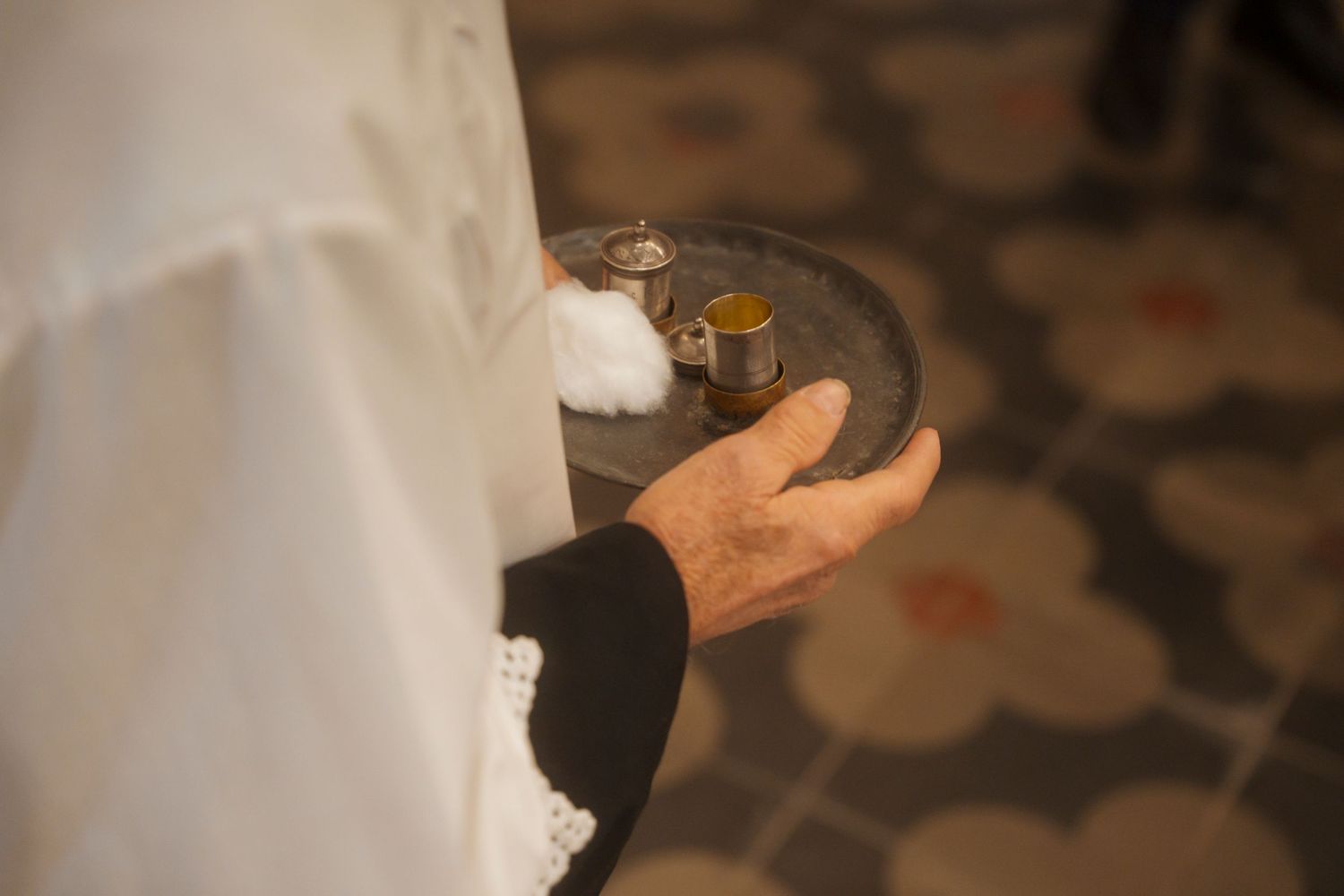 Priest holding ceremonial tray with small golden vessels during religious baptism ceremony.