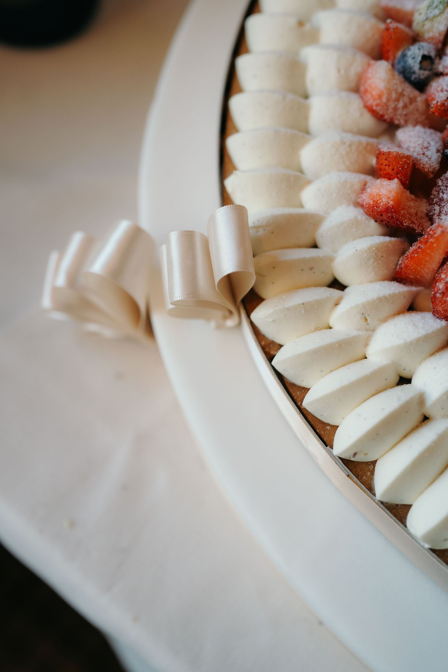 Close-up of a wedding cake decorated with rows of white cream, fresh strawberries, and a satin ribbon bow.