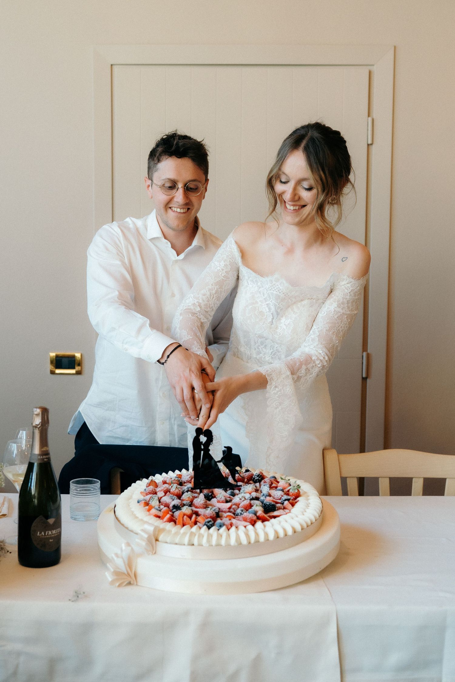 Happy couple cutting wedding cake topped with bride and groom figurine.