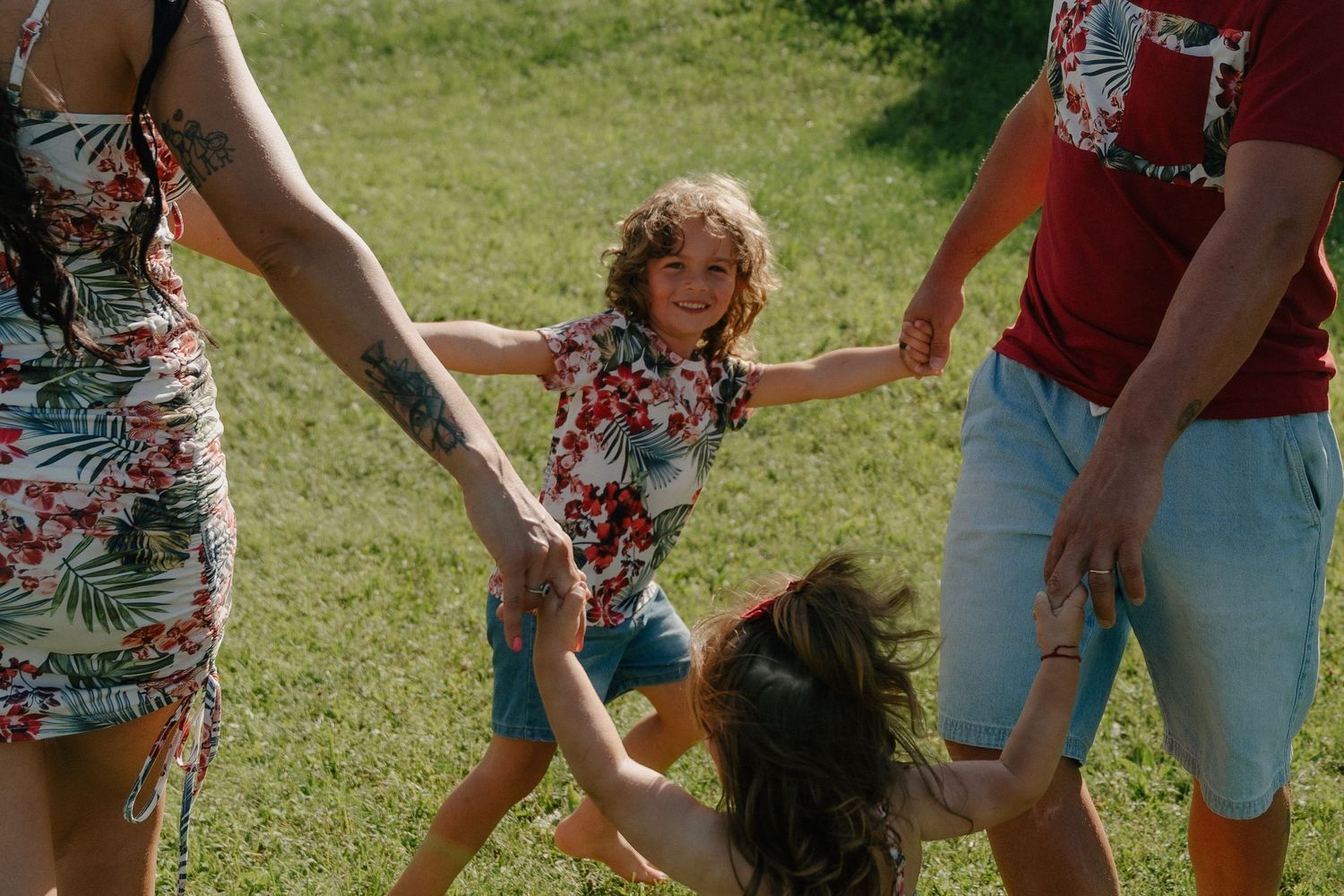 Una famiglia gioca all'aperto sull'erba verde: i bambini ridono mentre gli adulti si tengono per mano in un gioioso girotondo.