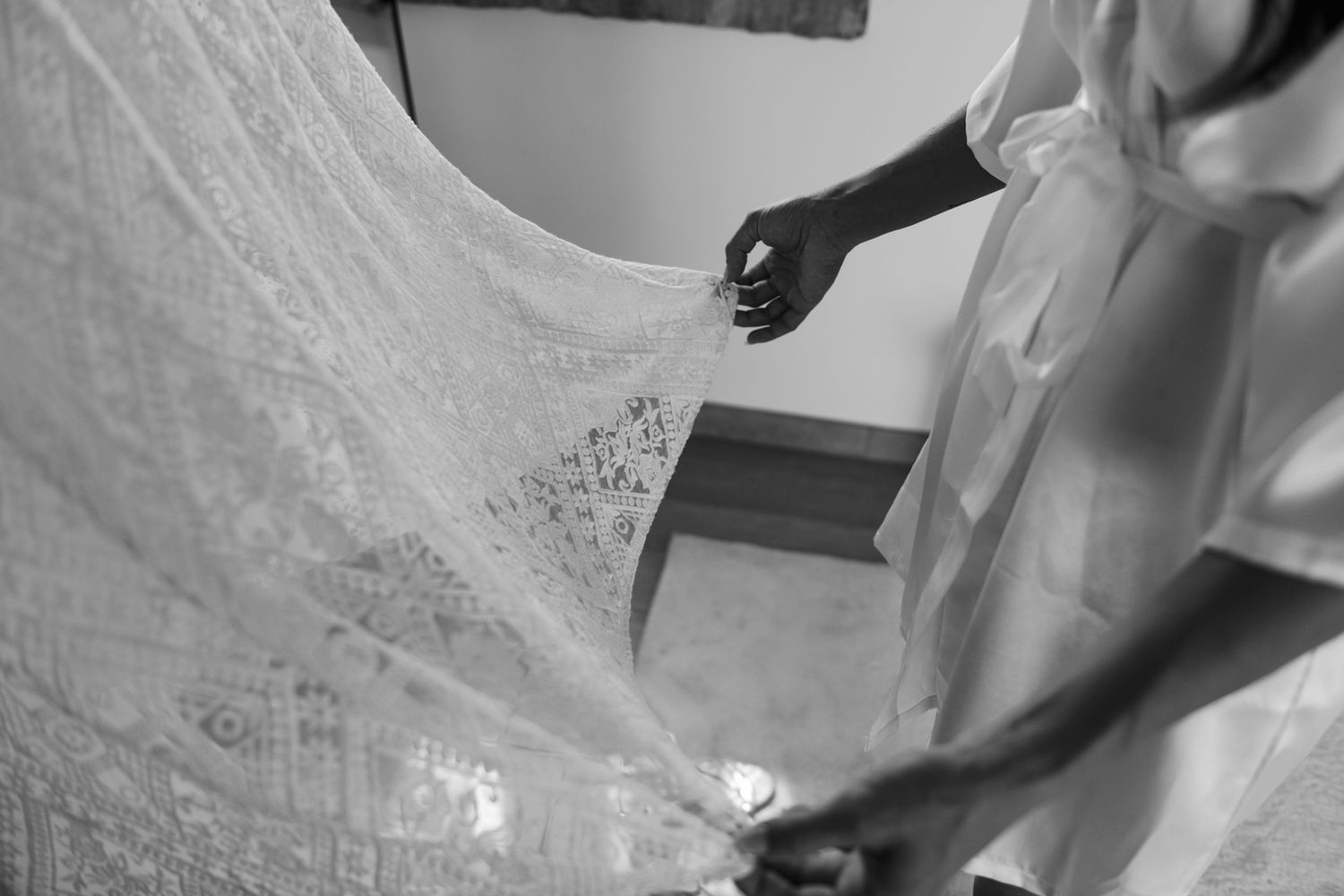 Black and white photo of hands holding delicate lace wedding veil before ceremony.