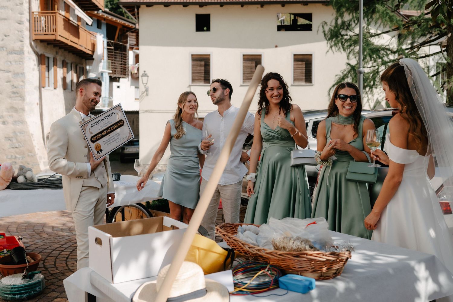 Bride in white gown with bridesmaids in sage green dresses celebrating outdoors at a rustic wedding venue.