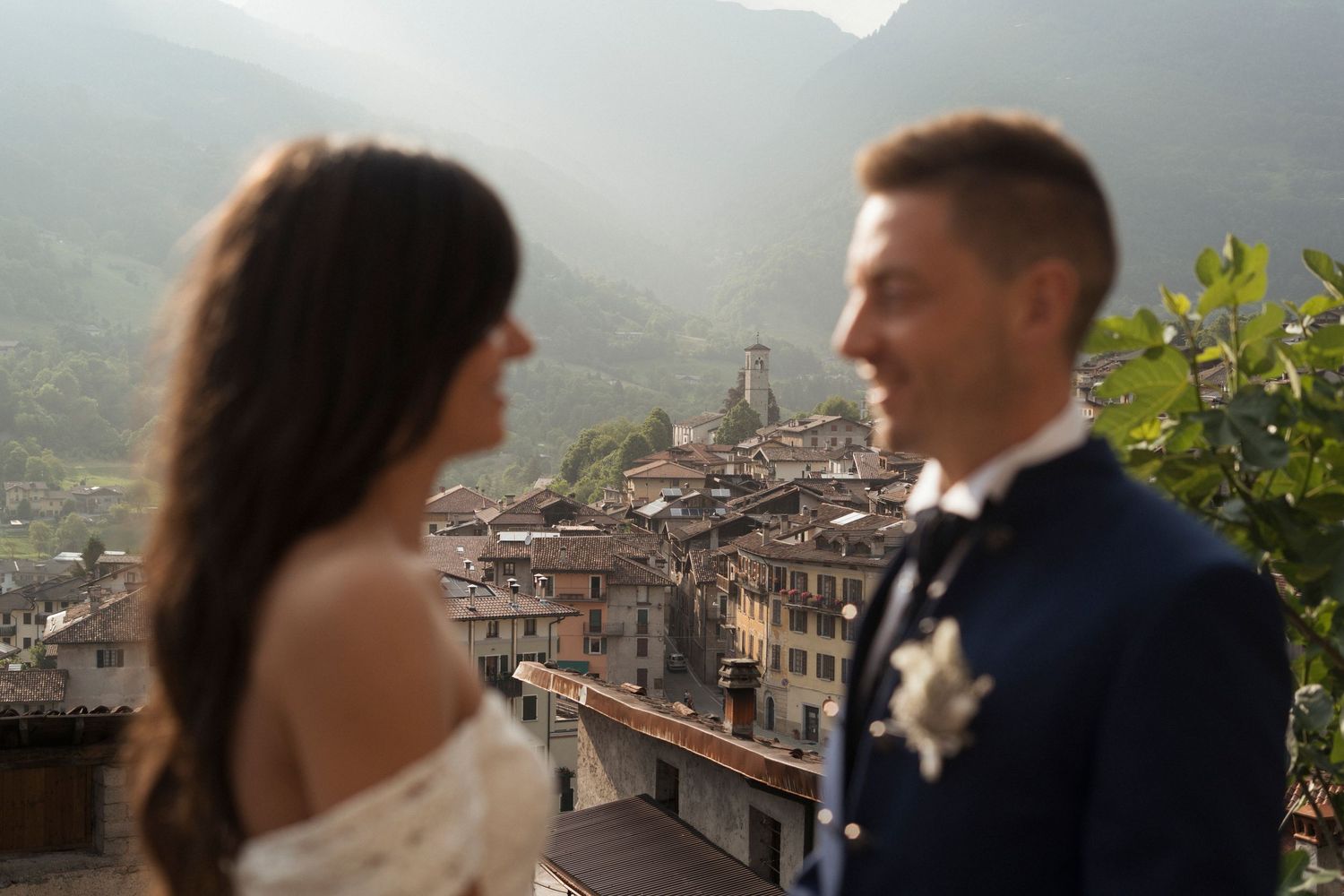 Bride and groom sharing romantic moment with scenic Italian hilltop village in background.