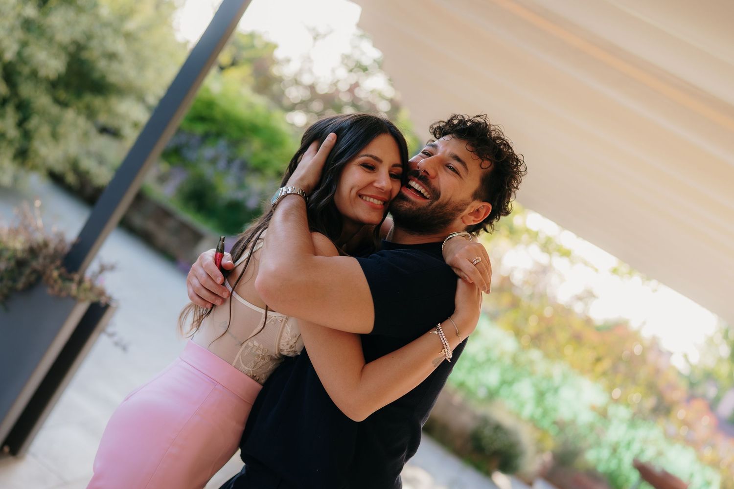 Joyful couple embracing and smiling outdoors in warm sunlight at a casual event.