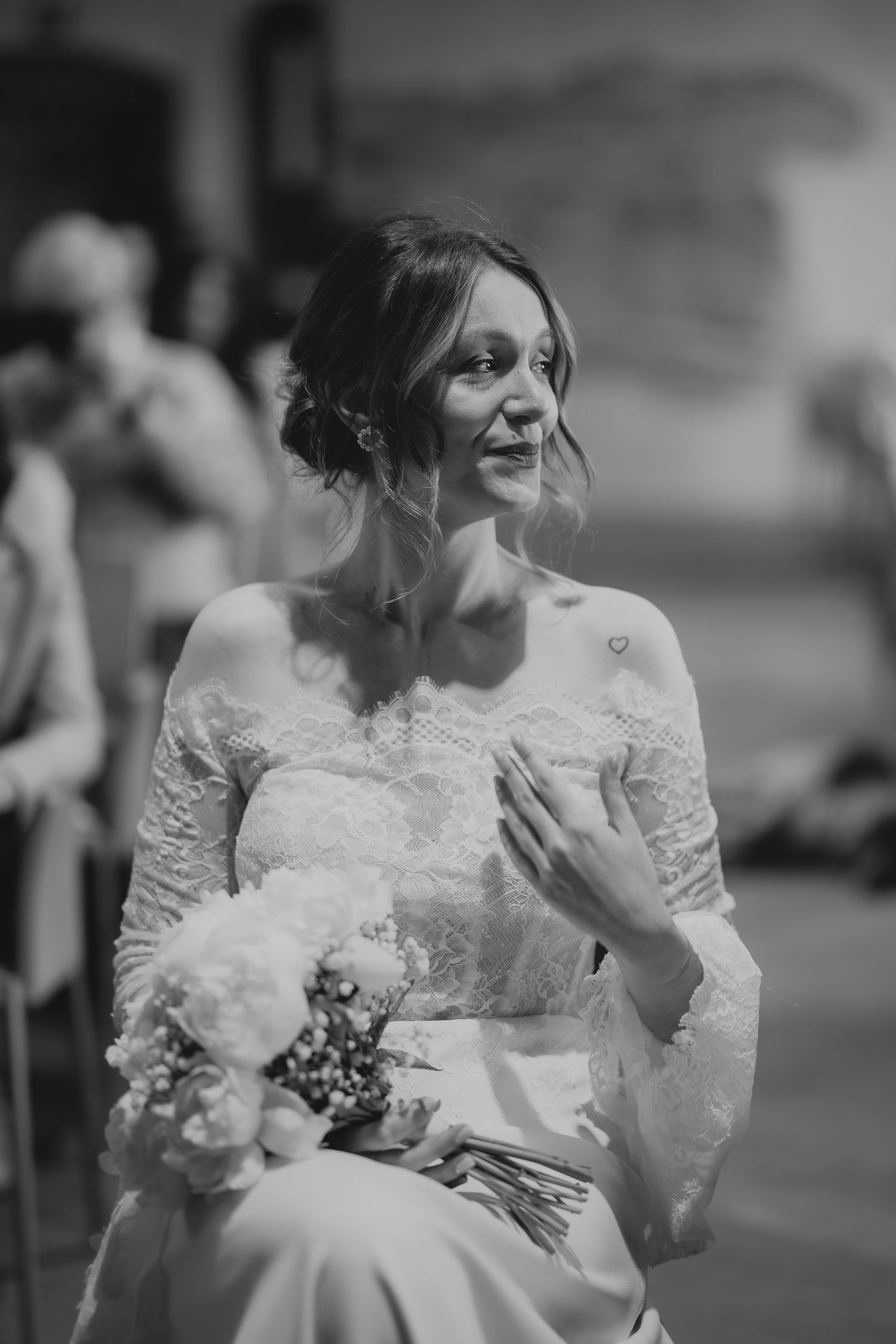 Emotional bride in lace wedding dress holding a white bouquet, captured in a candid black and white portrait.