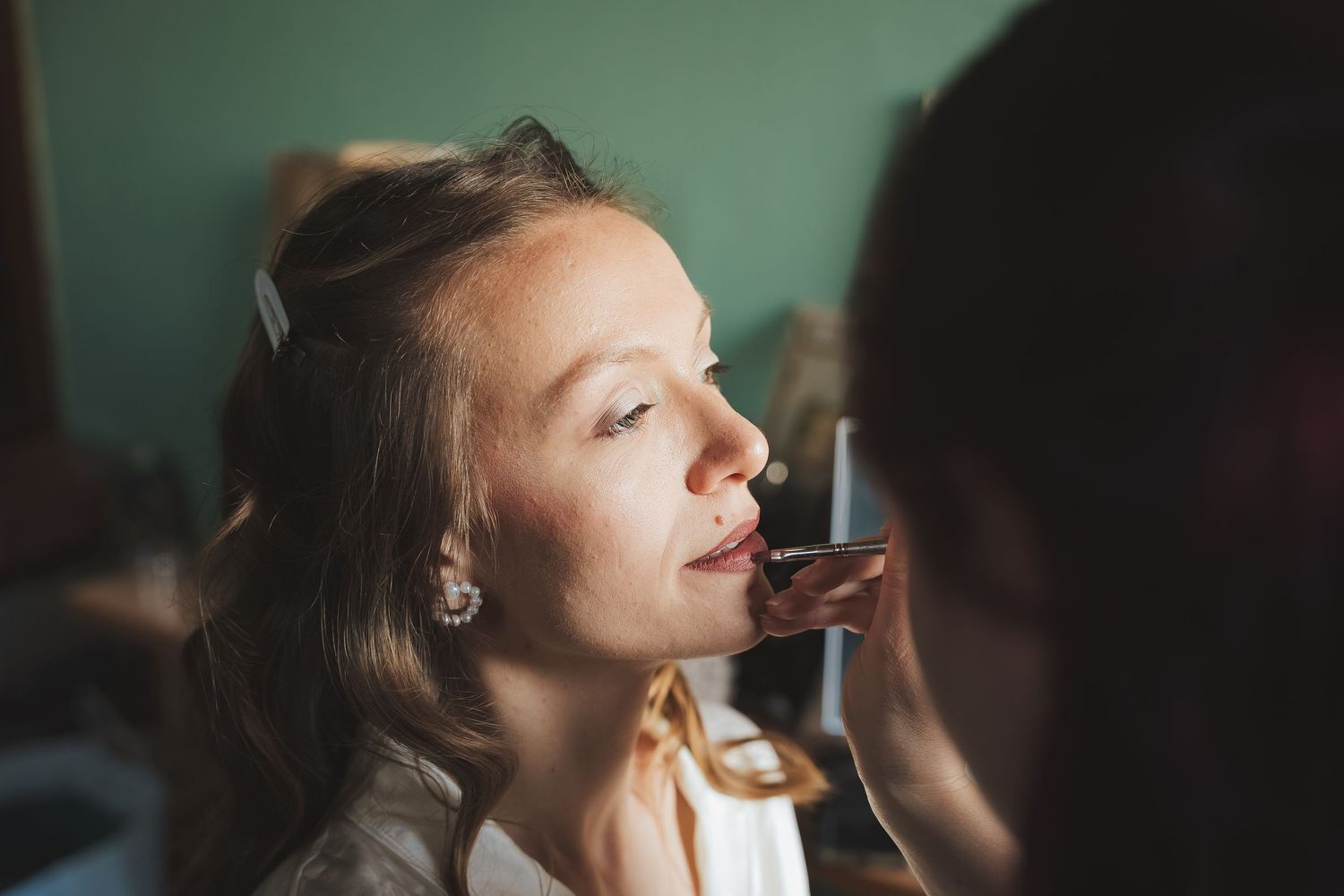 Bride getting makeup applied by artist before wedding ceremony, close-up beauty preparation shot.