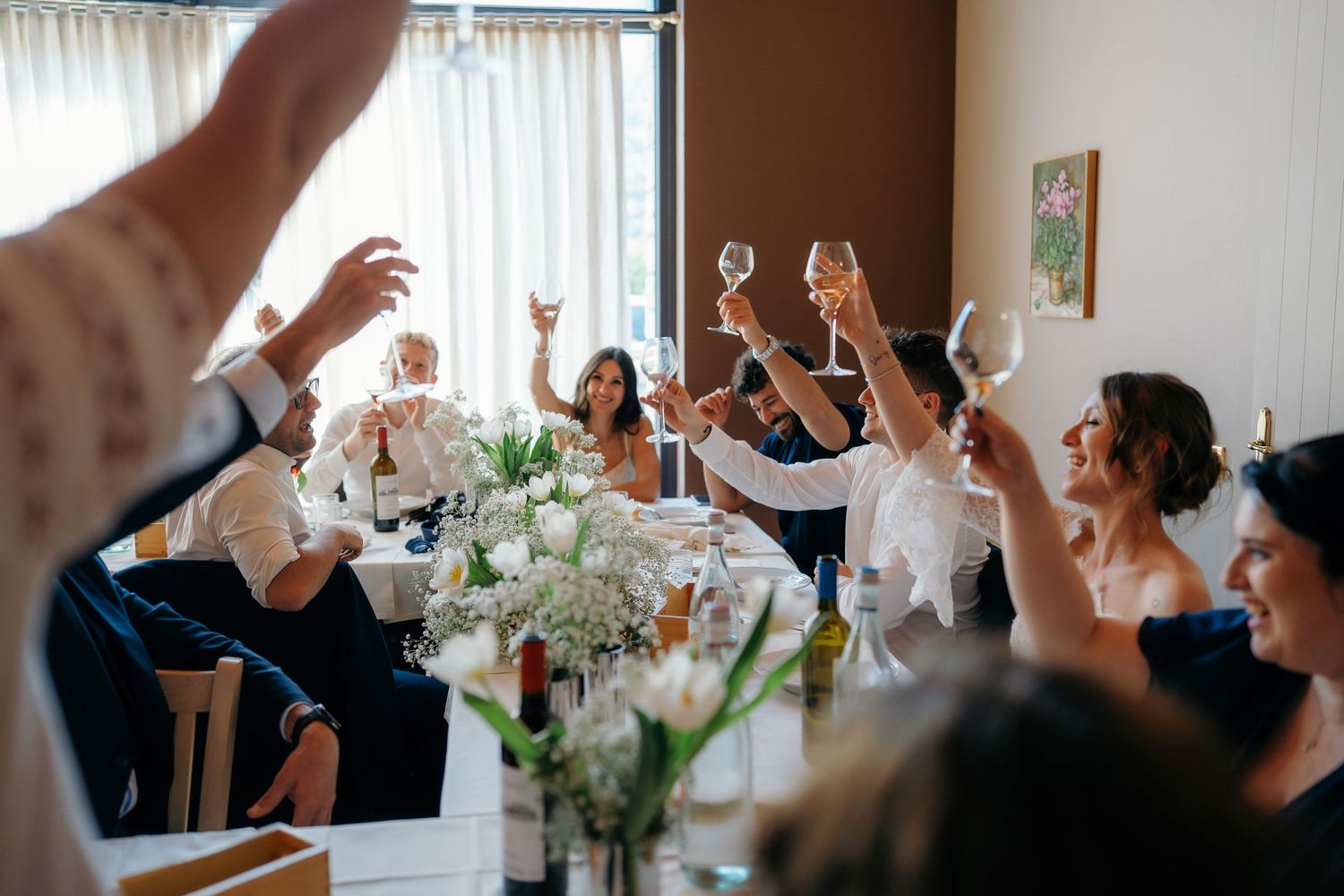 Wedding guests raise champagne glasses in joyful toast at elegant reception dinner table.