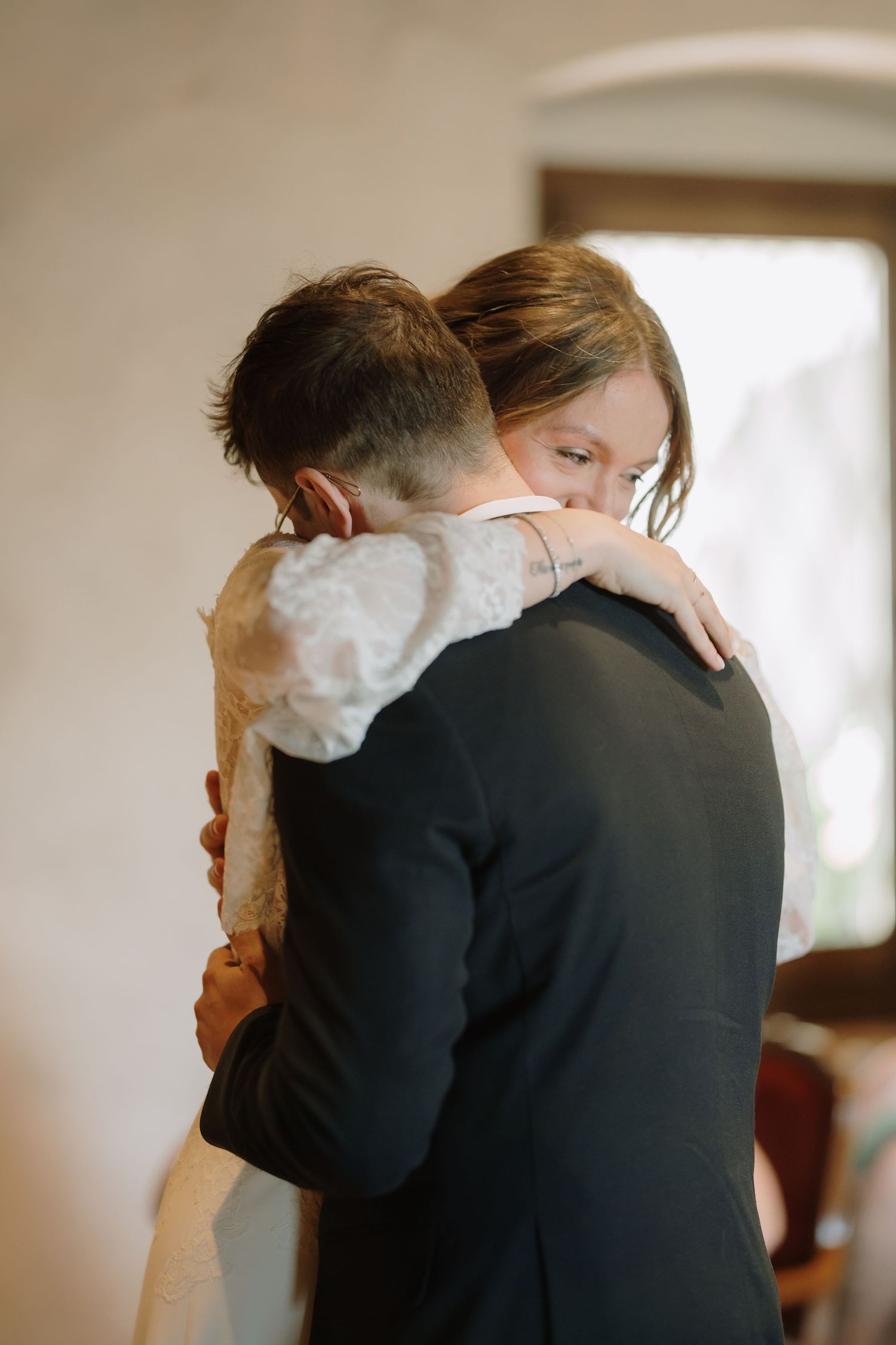 Bride and groom share an emotional embrace during their wedding ceremony, with the bride in a lace dress hugging the groom.