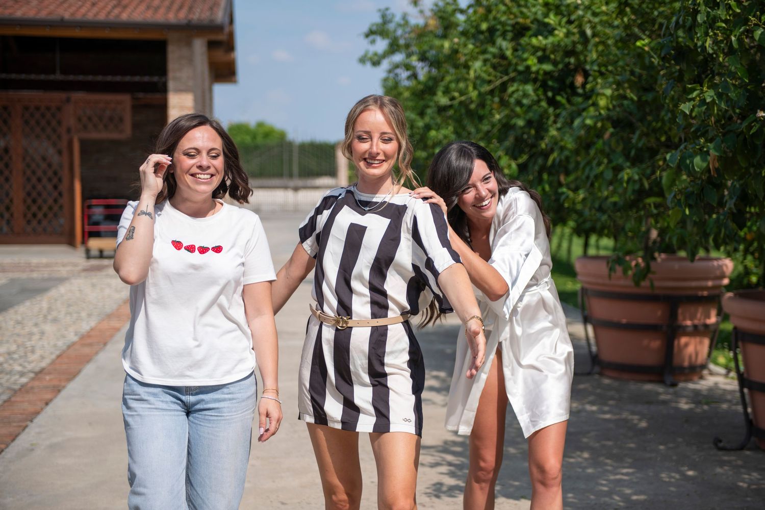 Three women walking and laughing outdoors, wearing casual summer outfits on a sunny day.