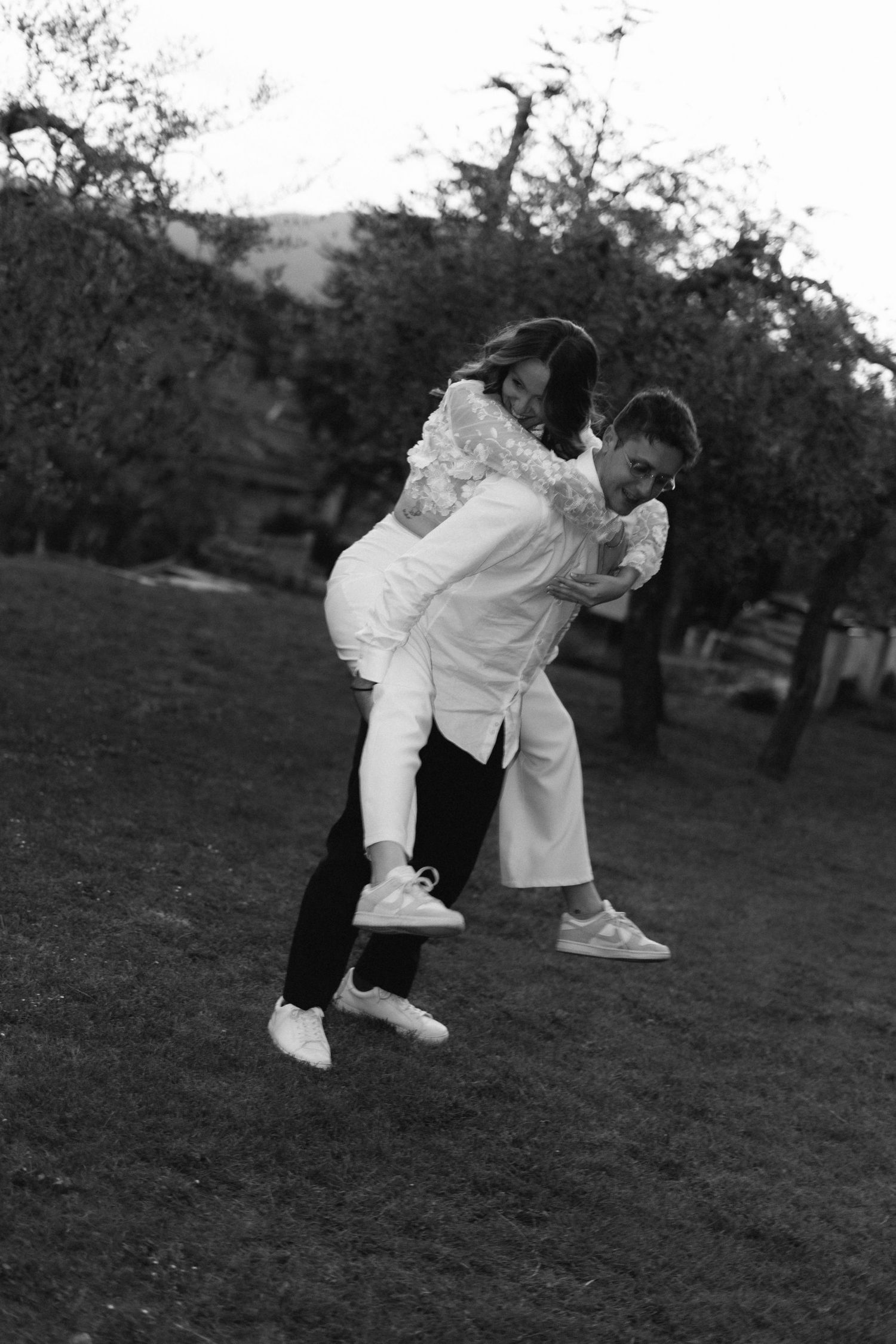 Foto in bianco e nero di uno sposo che solleva scherzosamente la sposa in un giardino durante i festeggiamenti del matrimonio.