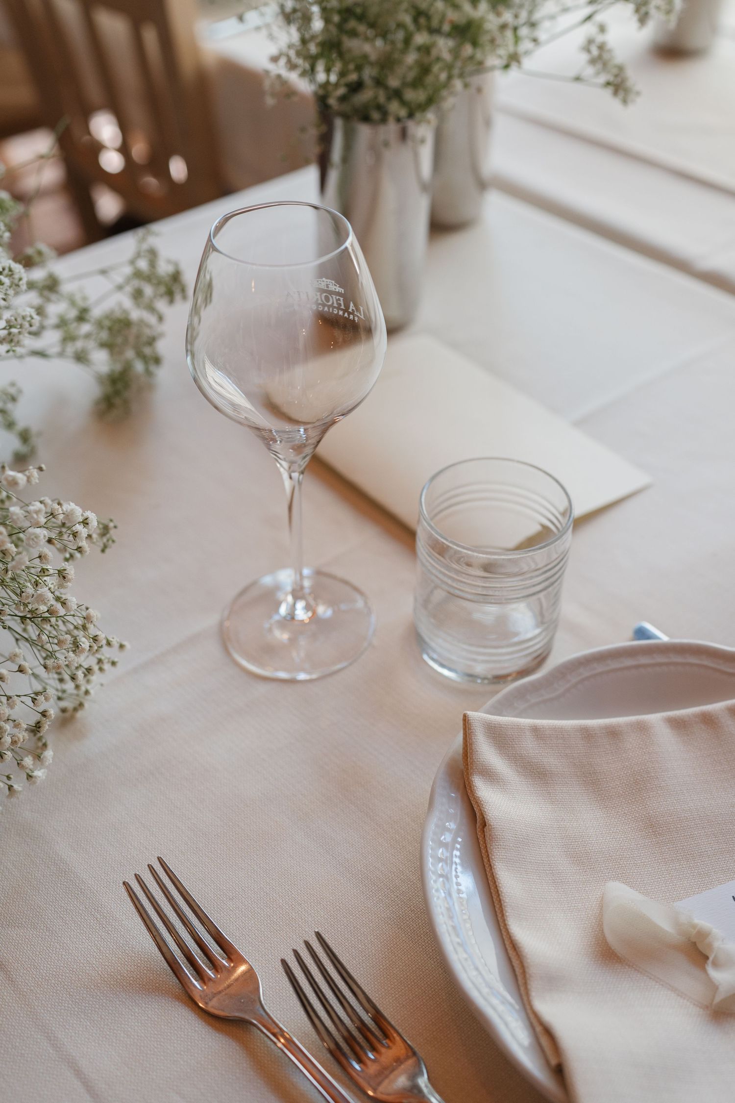 Primo piano di un'elegante mise en place nuziale con calice da vino, tovagliolo di lino, forchette e fiori