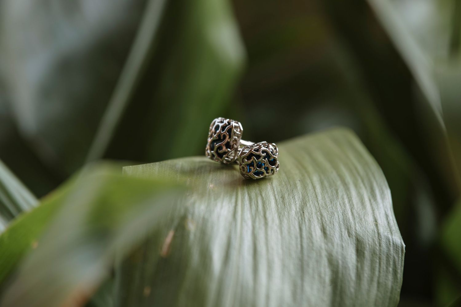 Delicate silver leopard print stud earrings resting on a lush green tropical leaf in a natural setting.