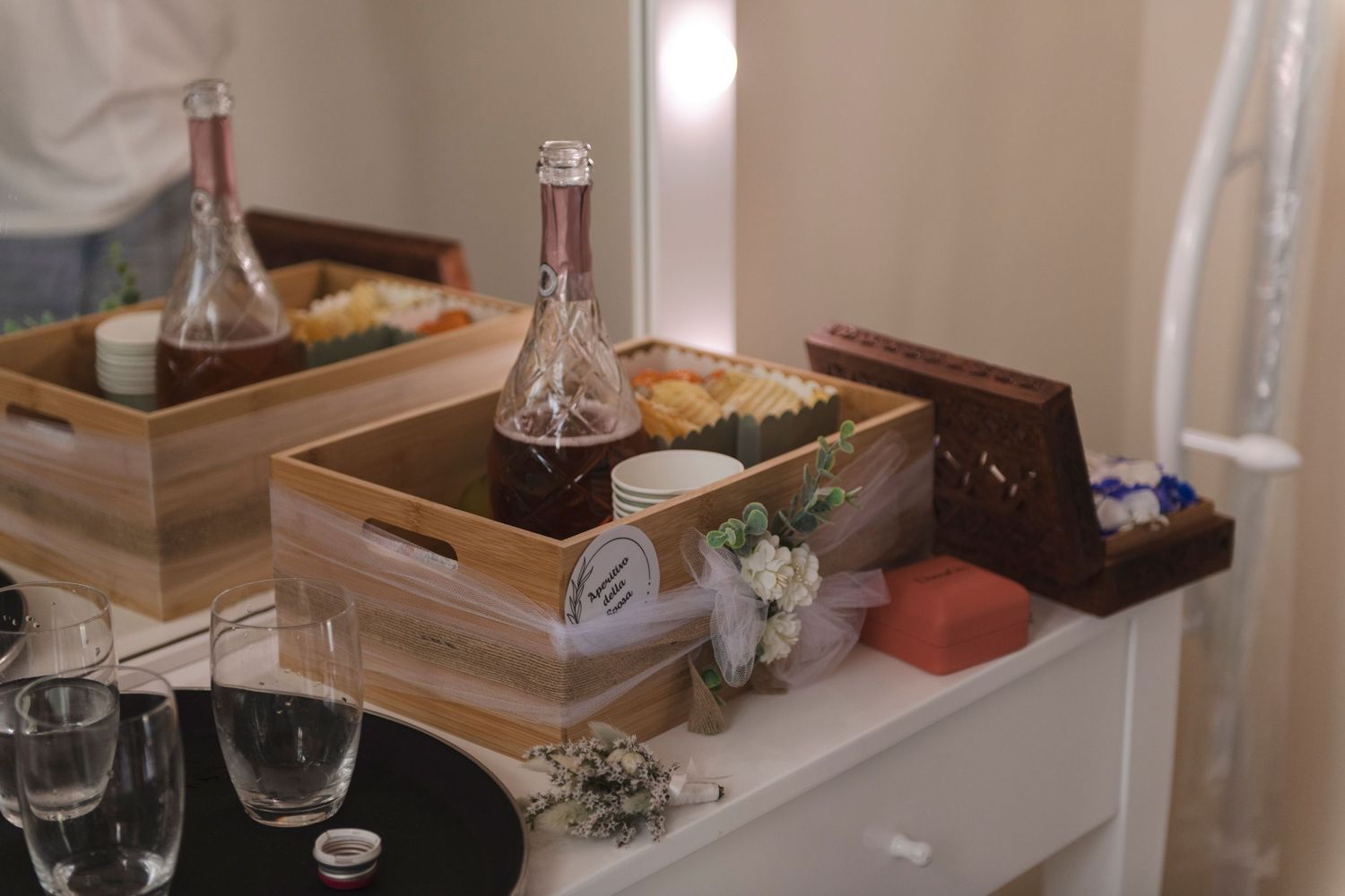 Wooden crates with wine bottles and decorative flowers displayed on a white dresser for an elegant event setup.