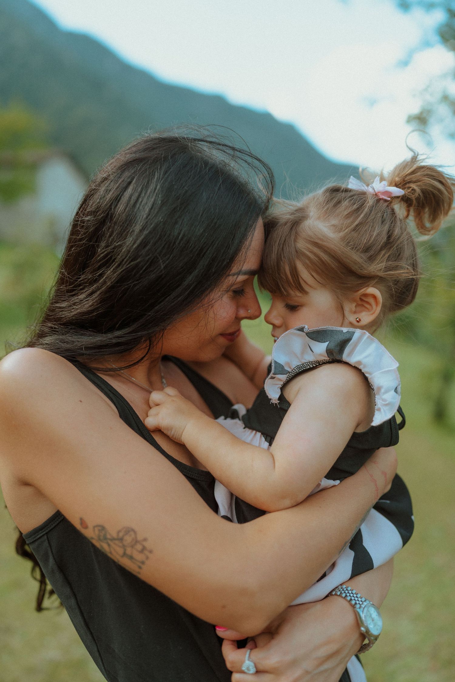 Una madre stringe teneramente a sé la giovane figlia, unendo le fronti in un abbraccio amorevole all'aperto.