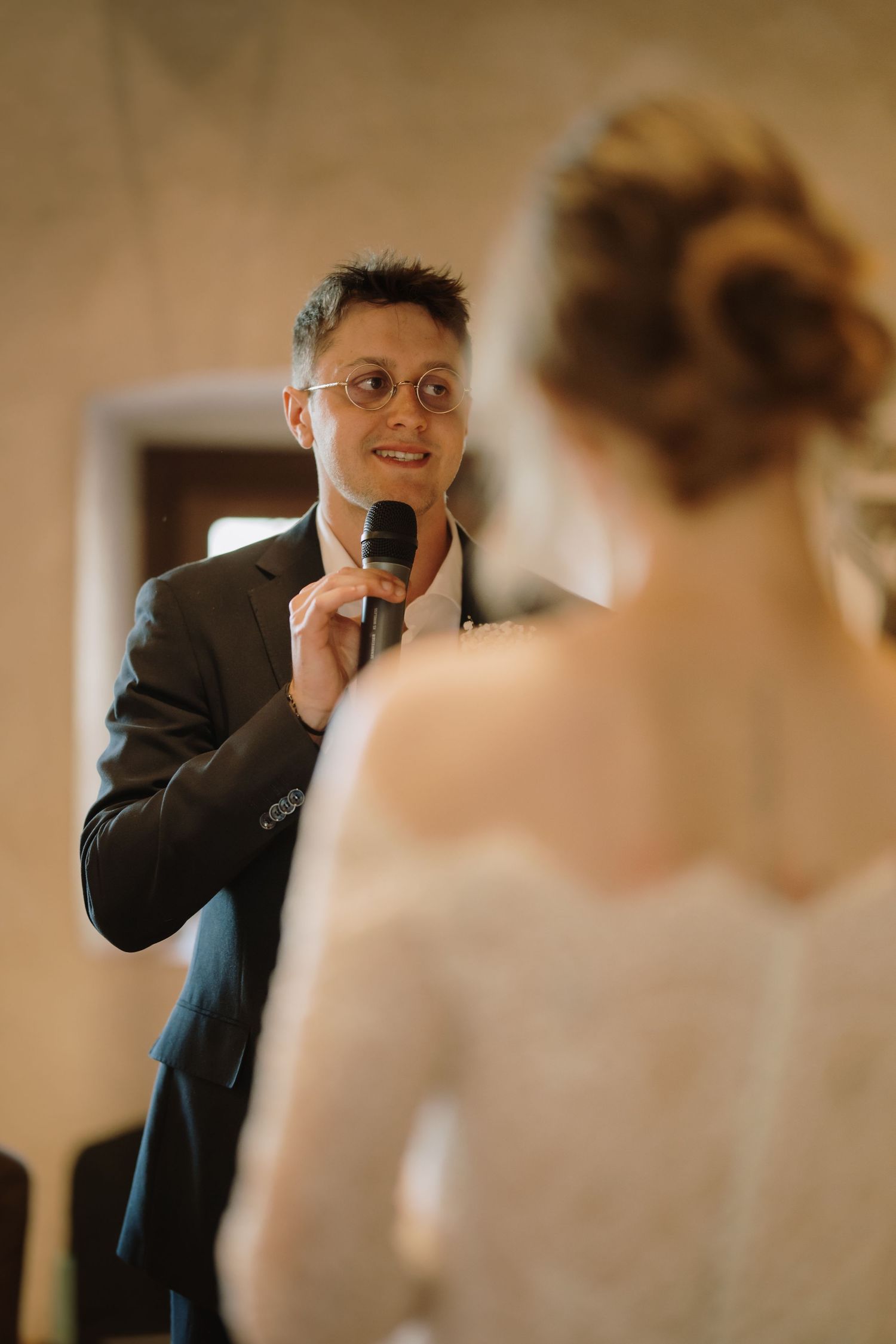 Groom reciting wedding vows into a microphone while looking lovingly at his bride during a wedding ceremony.