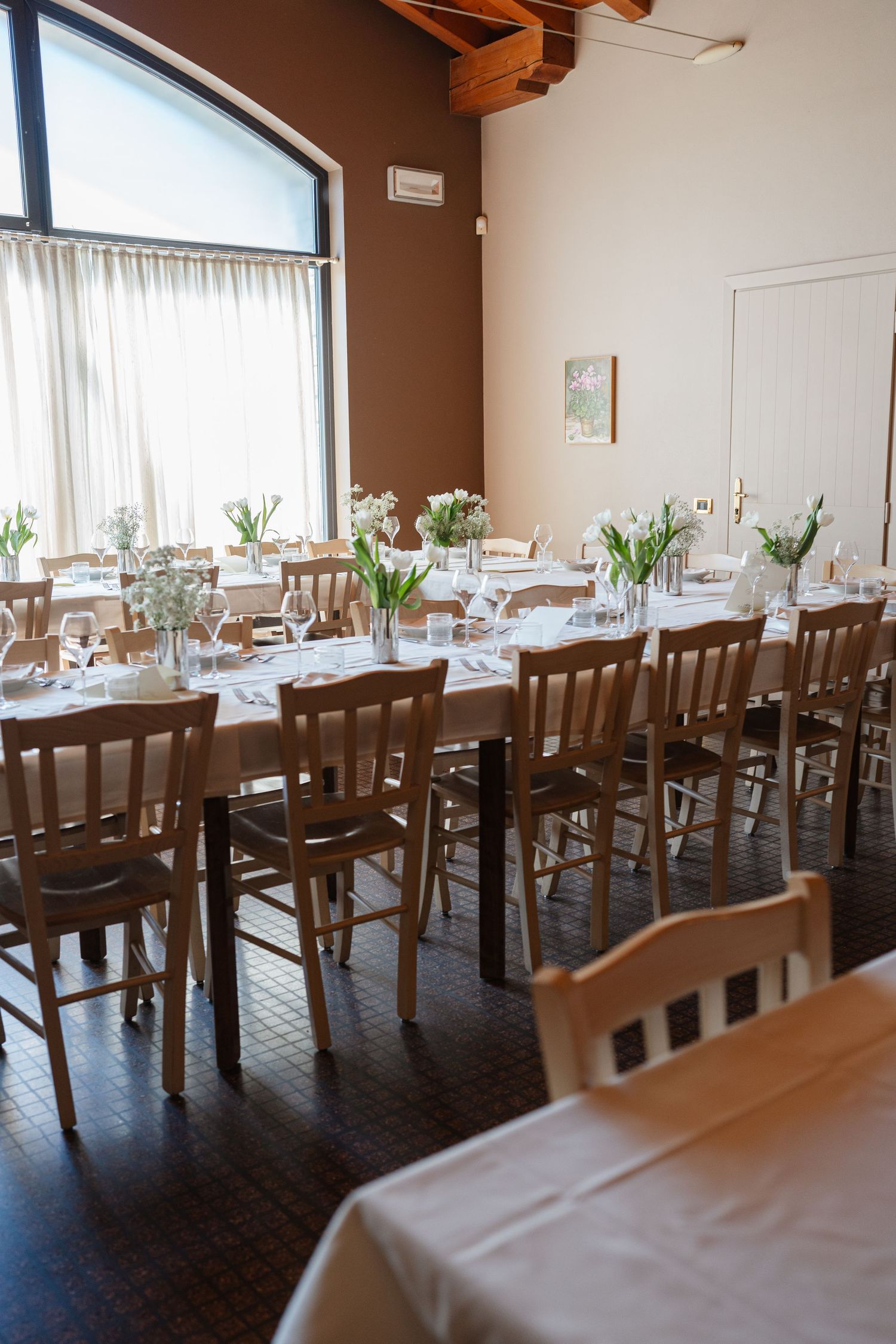 Elegant wedding reception venue with long tables, wooden chairs, white linens, and fresh tulip centerpieces.