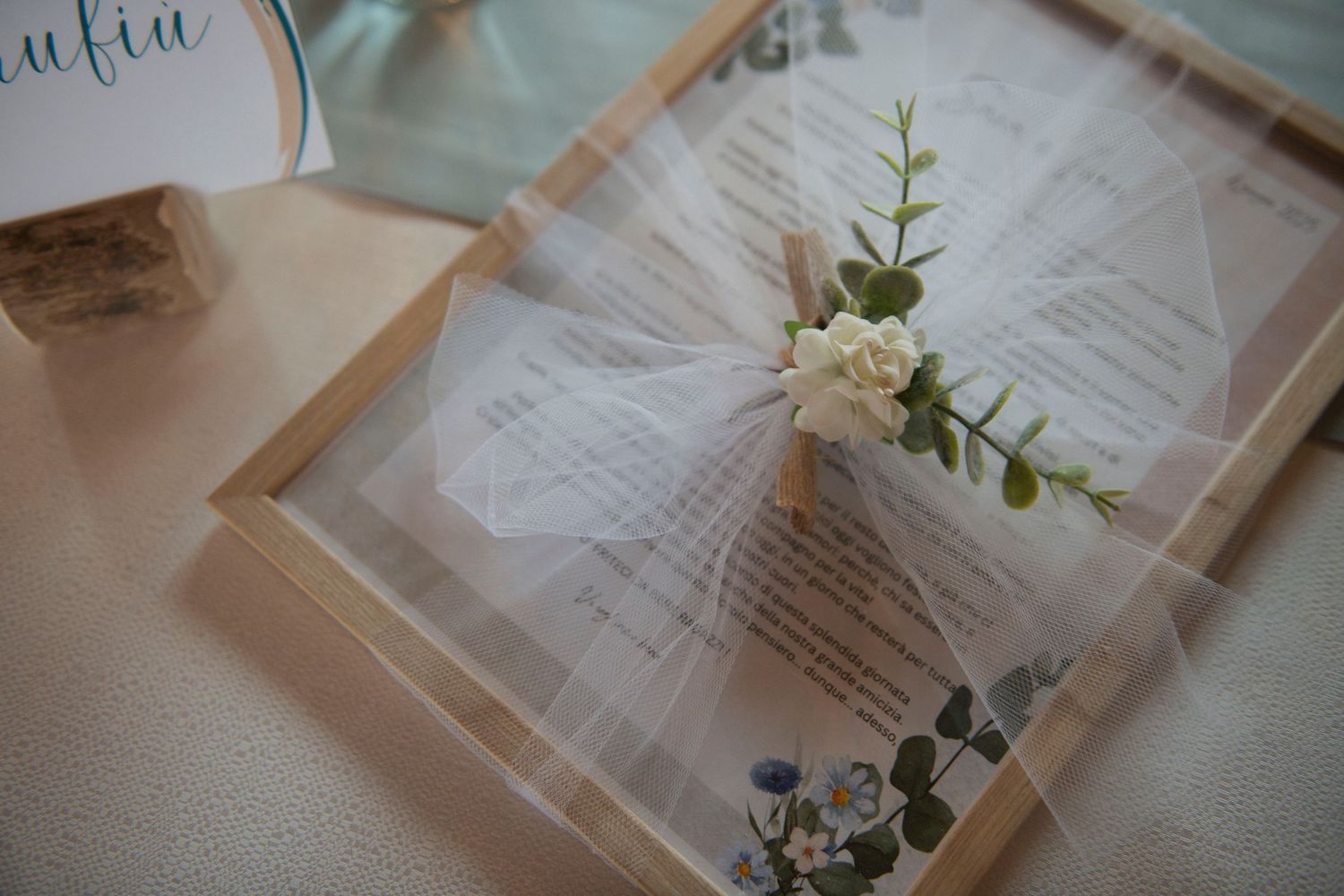 Decorative wedding invitation wrapped in tulle with a white flower and eucalyptus sprig accent.