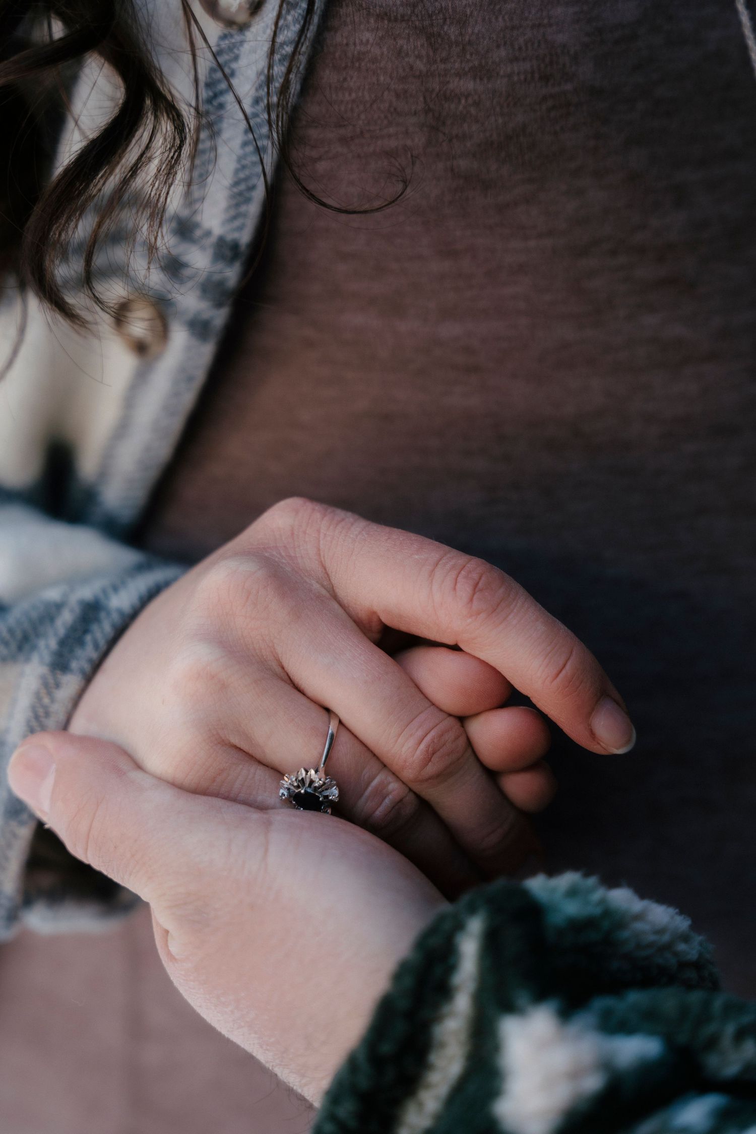 Close-up of woman's hand wearing an elegant floral diamond engagement ring over winter outfits.