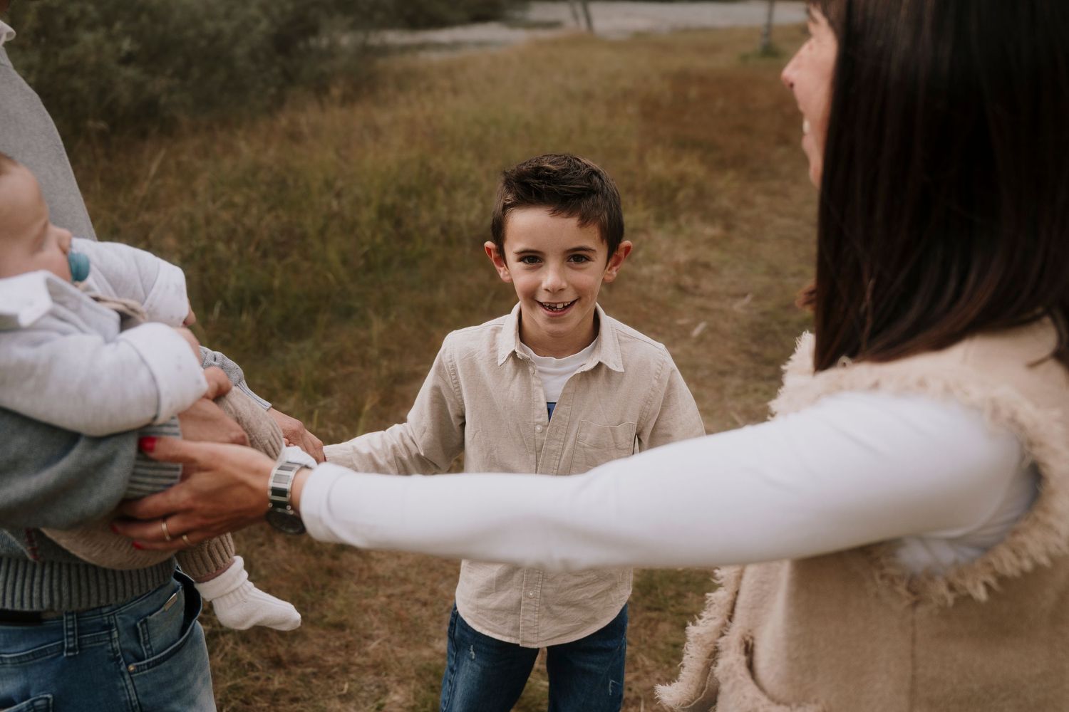 Smiling young boy holding hands with parents in an outdoor autumn field setting.