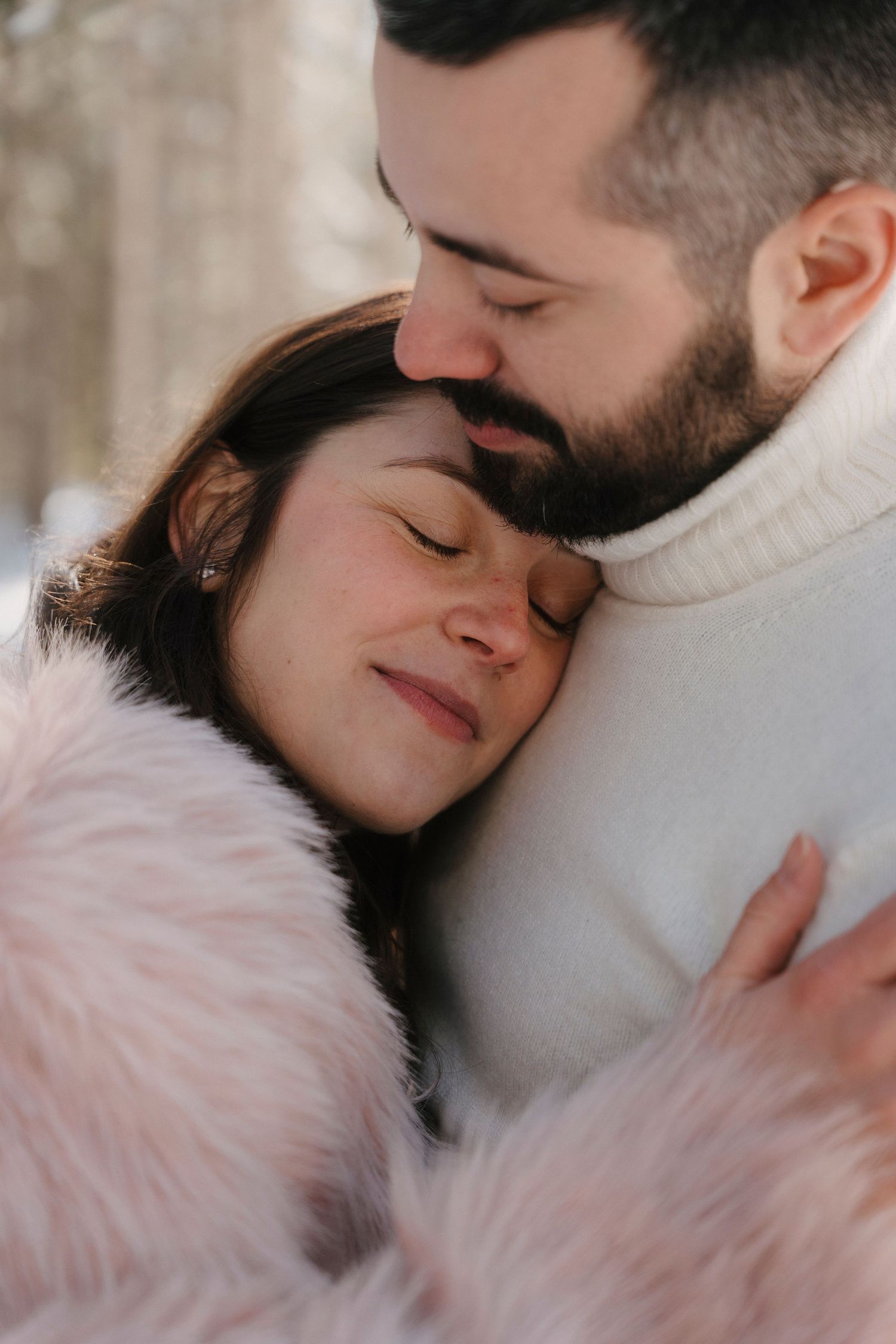 Tender moment of couple embracing, woman in pink fur coat resting head on man's chest.