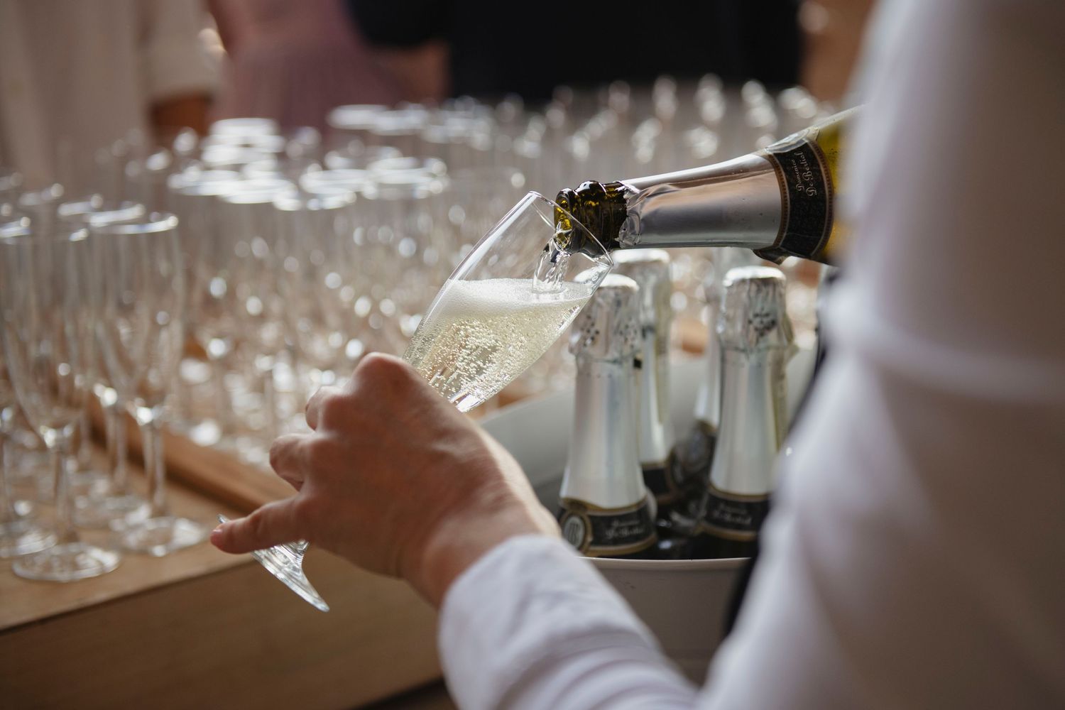 Champagne being poured into glass at wedding reception with rows of glasses in background.
