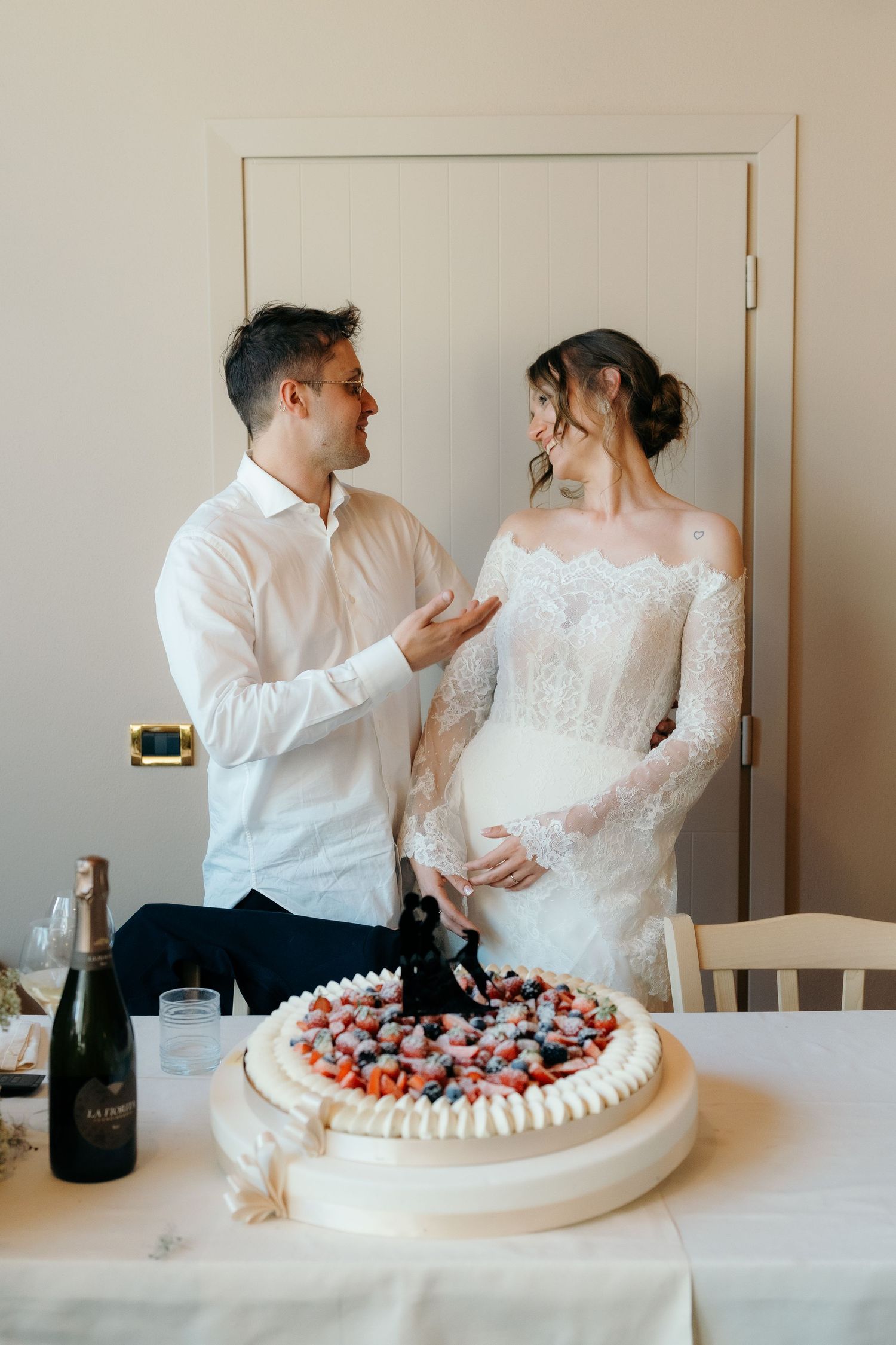 Bride and groom share a tender moment beside their elegant white wedding cake topped with fresh berries.