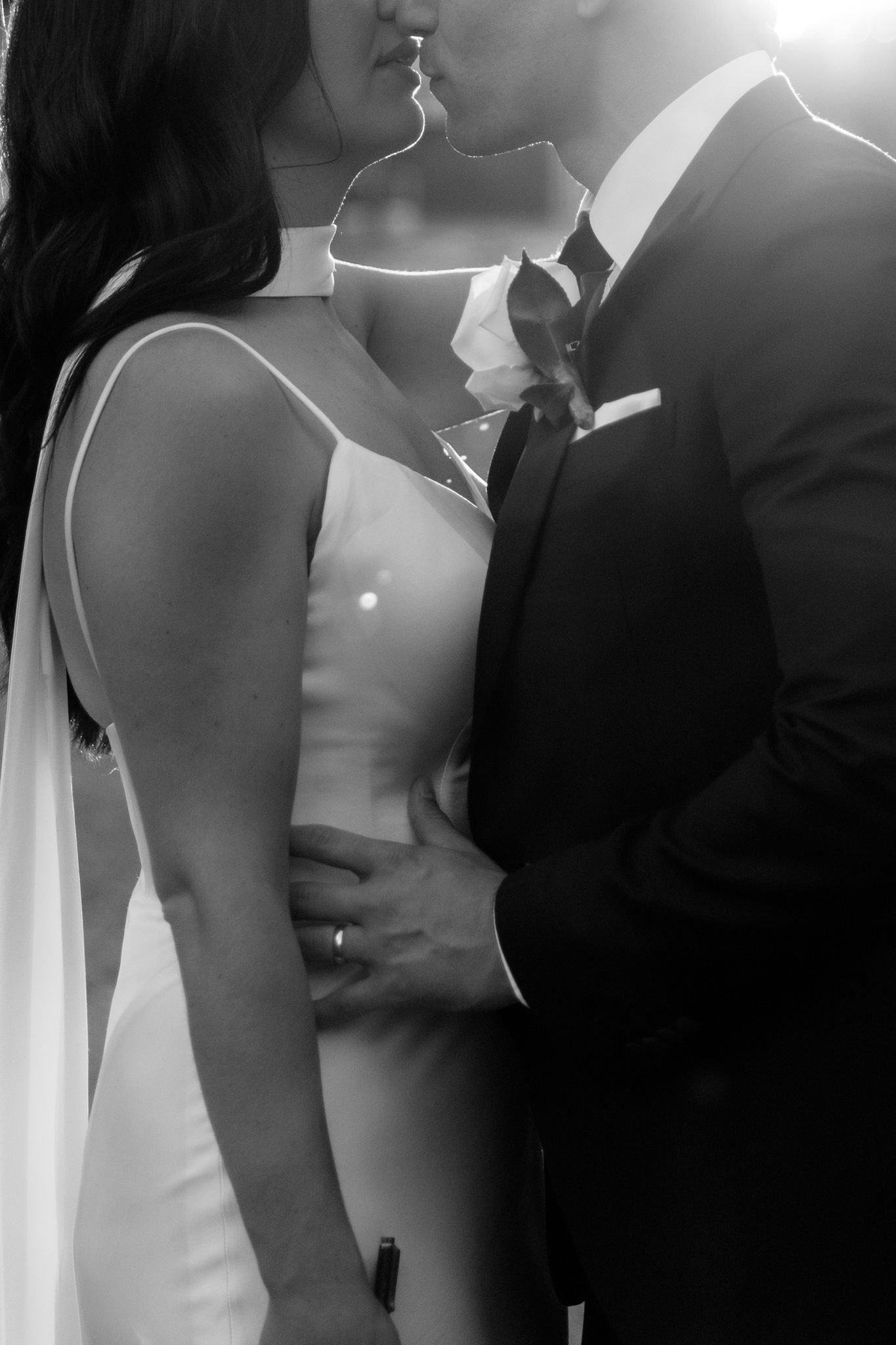 Black and white intimate wedding photo showing silhouette of couple in formal attire sharing a romantic moment.