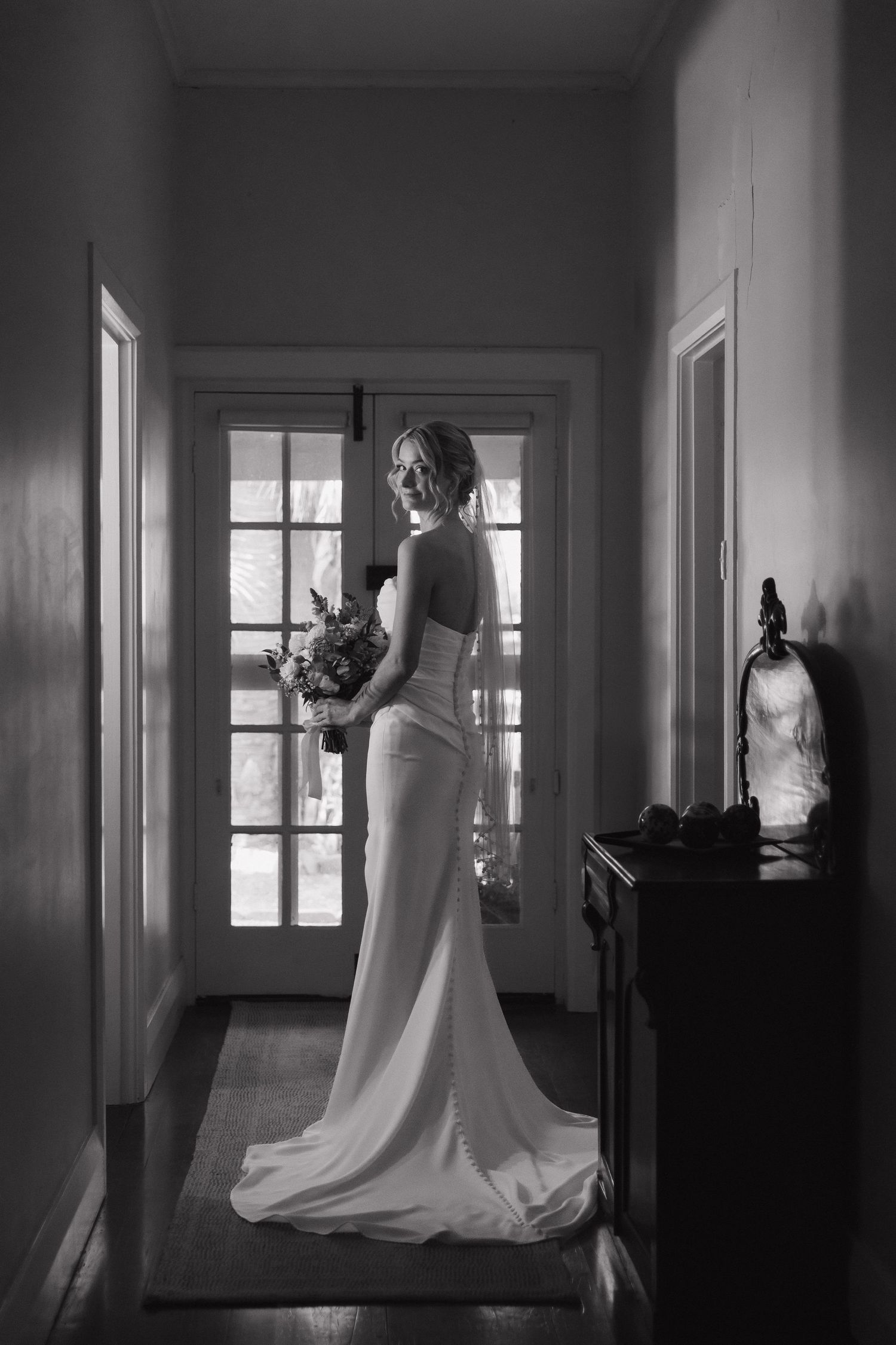 Silhouette of a bride holding bouquet while standing in a hallway with french doors.