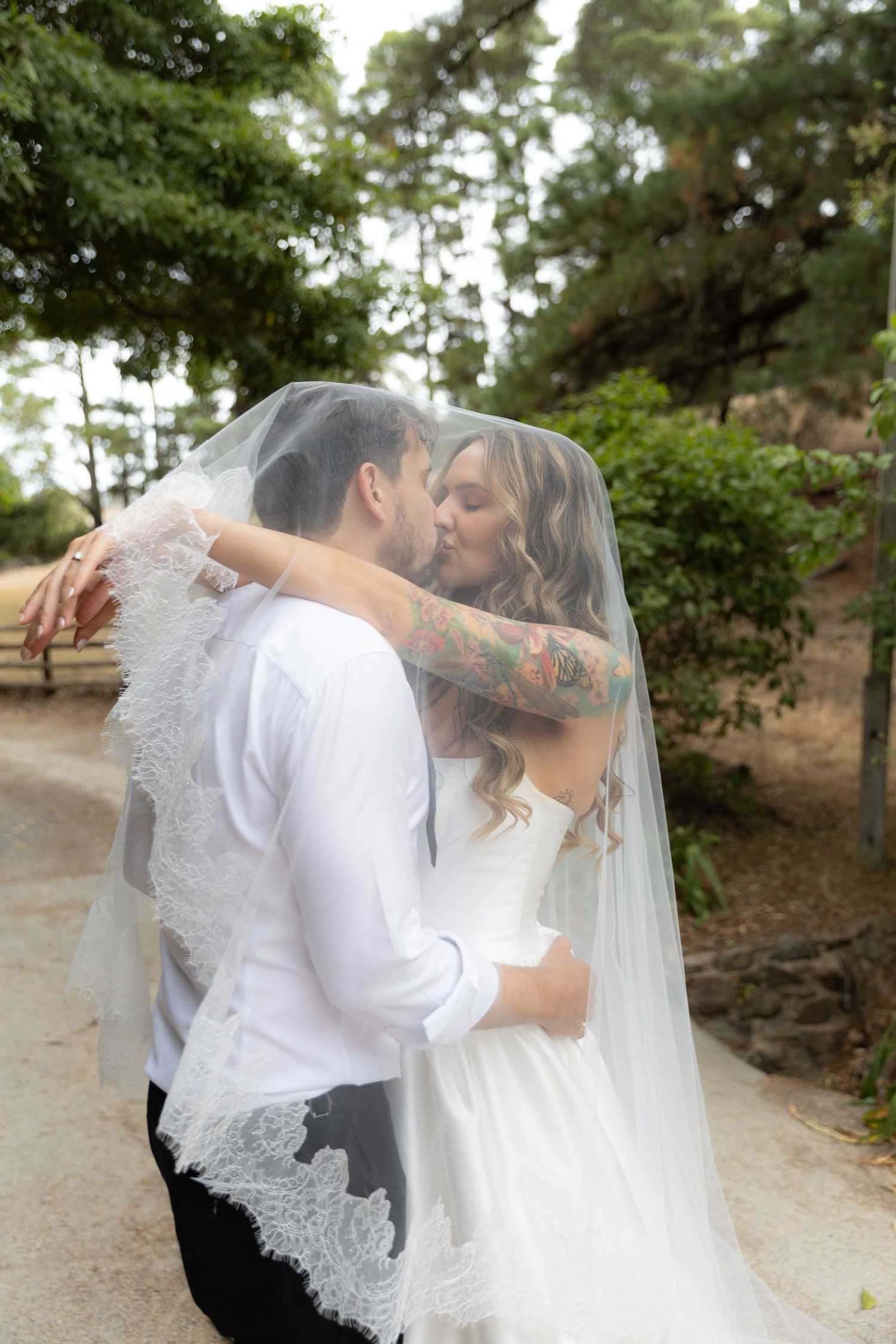 A romantic wedding moment captured under a veil as the couple shares their first kiss on a garden path.