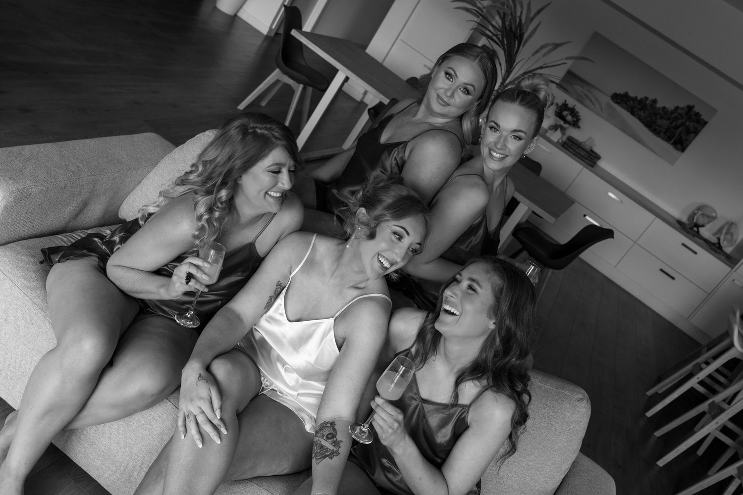 A group of people laughing together while sitting on a couch in a casual indoor setting, captured in black and white.
