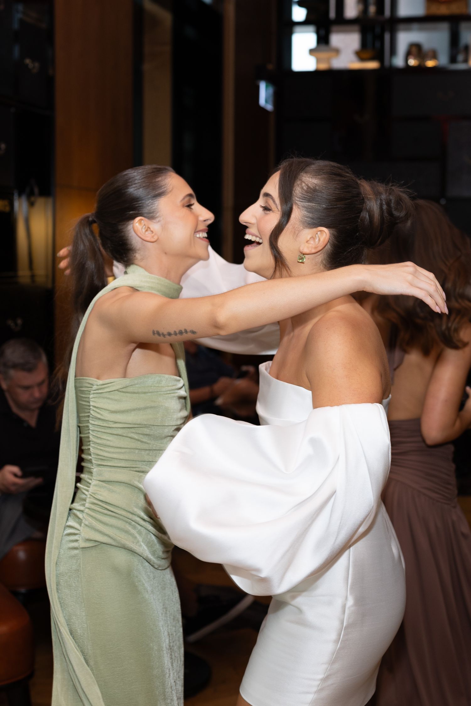 Two friends in formal dresses share joyful embrace at celebration.