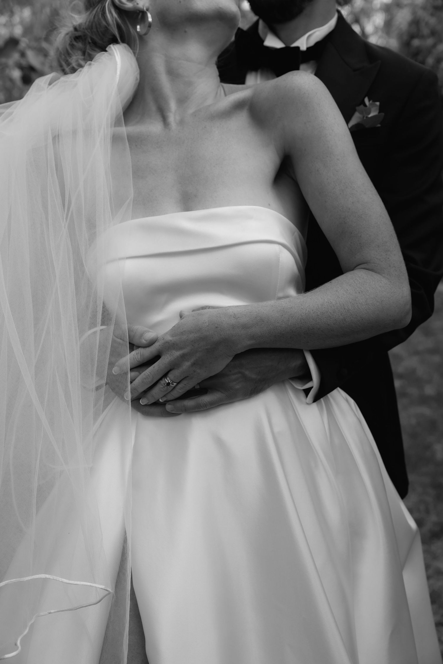 Black and white close-up of a bride in a strapless wedding dress with flowing veil.