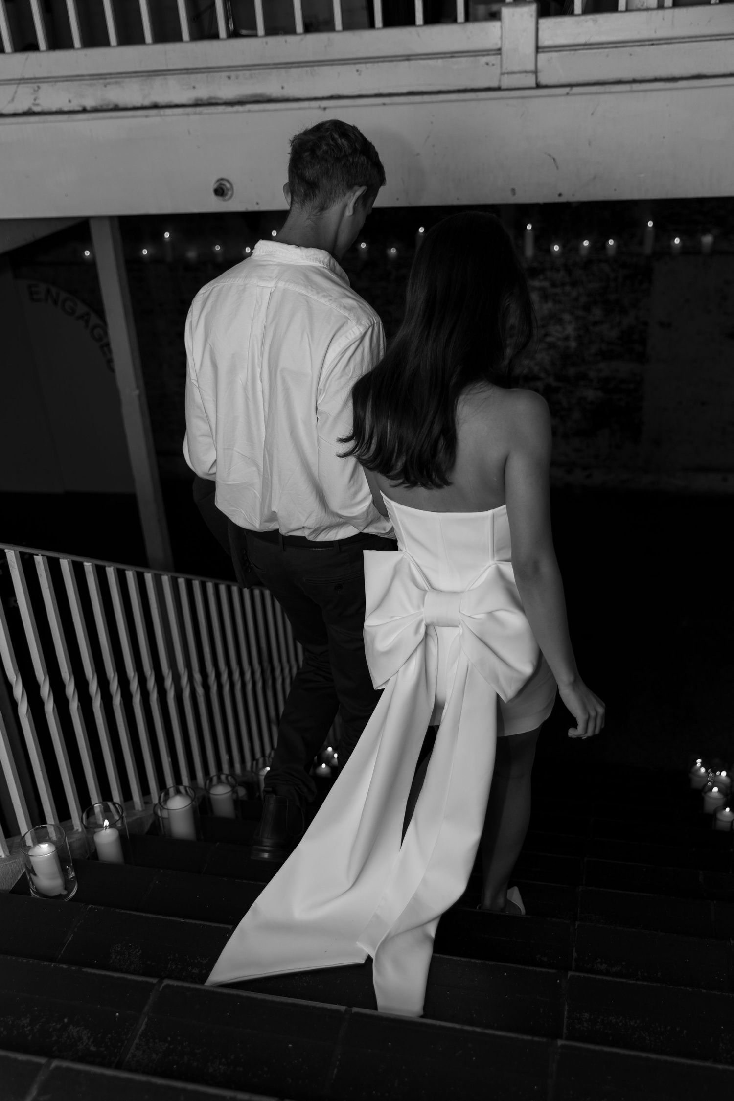 A black and white photo of a couple descending stairs lined with glowing candles.