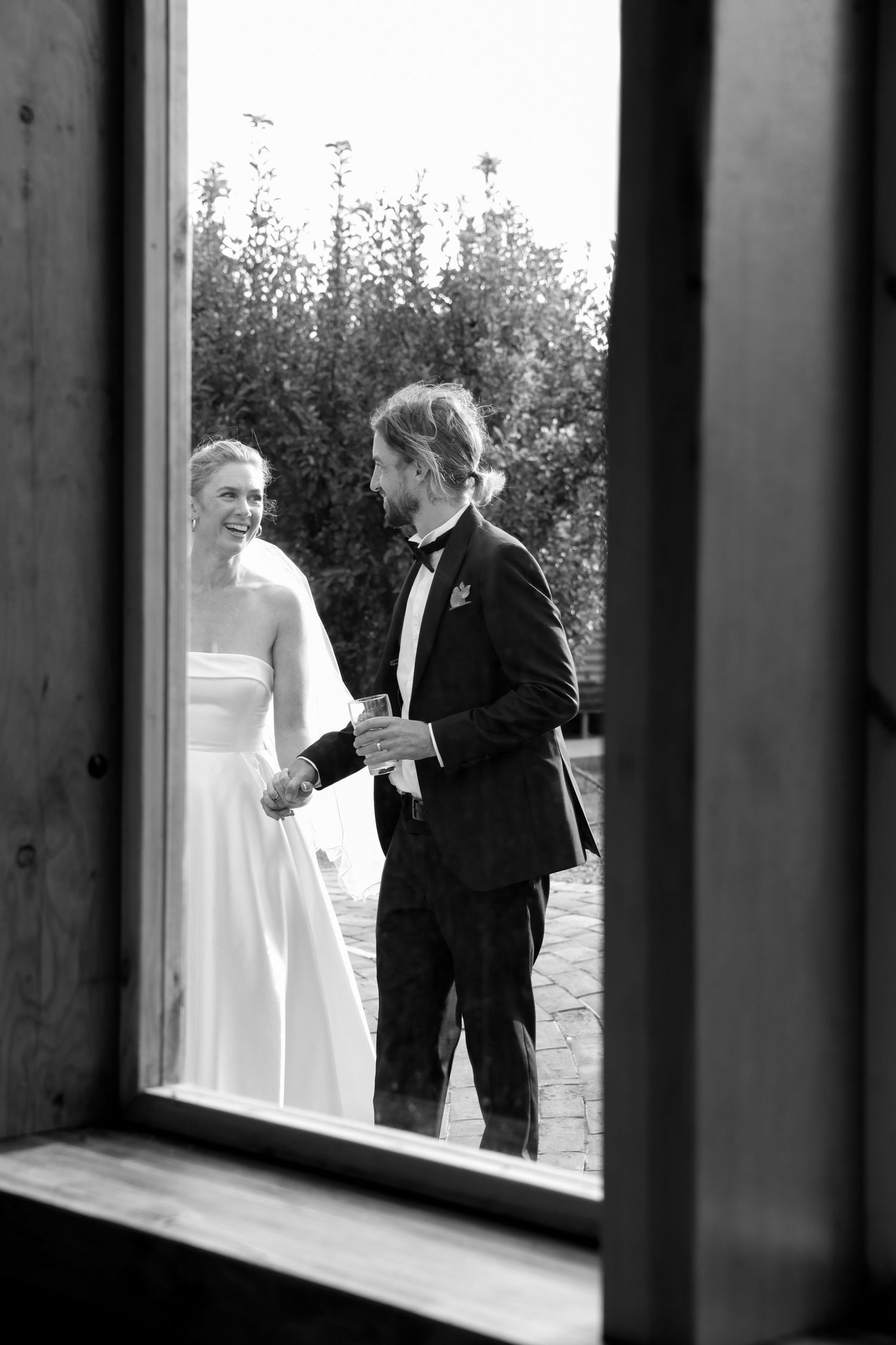 Black and white photo through a window frame of a wedding moment.