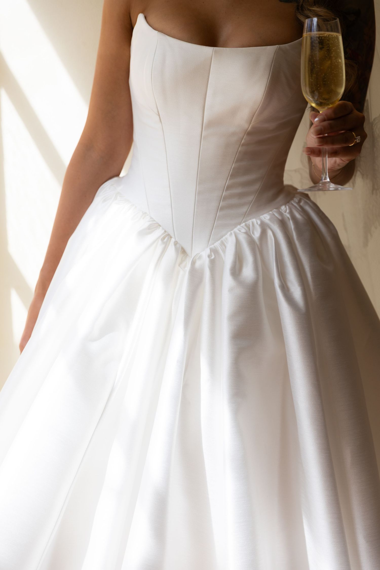 Close-up of white wedding dress bodice and full skirt with champagne glass.