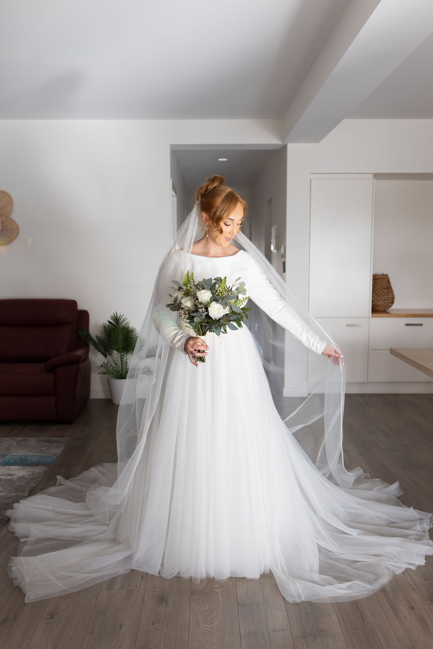 A flowing white wedding gown with a dramatic cathedral-length train sits elegantly in a light-filled modern interior space.