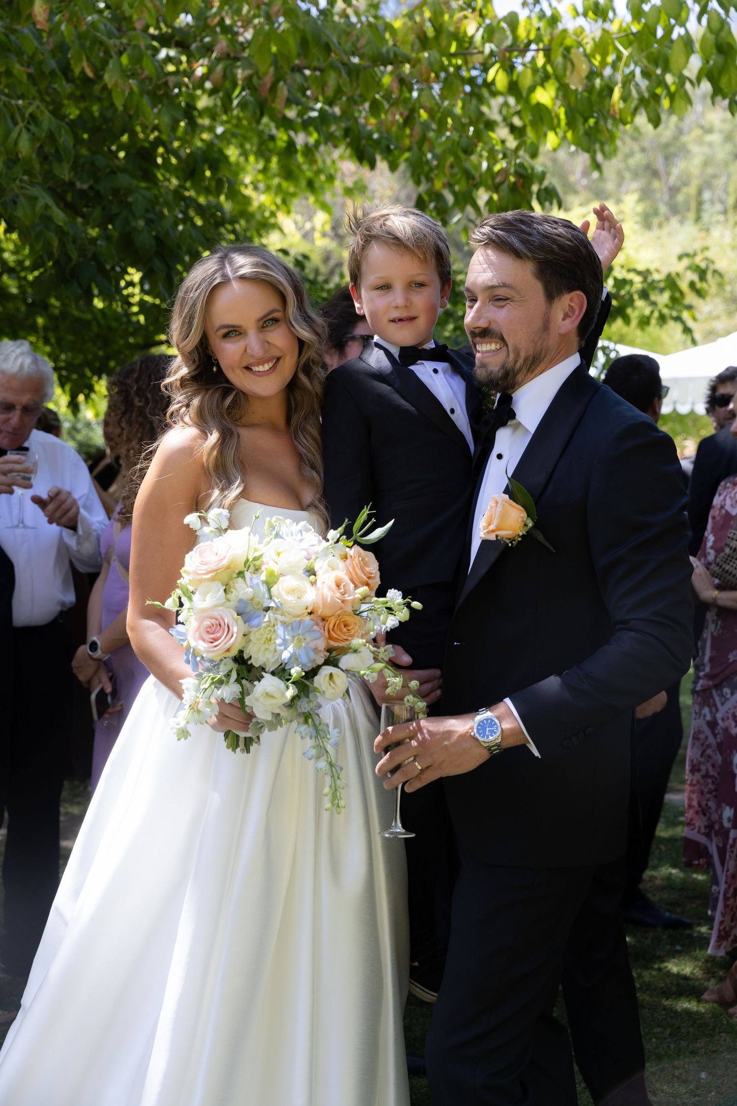 Joyful wedding photo of couple with young ring bearer outdoors.