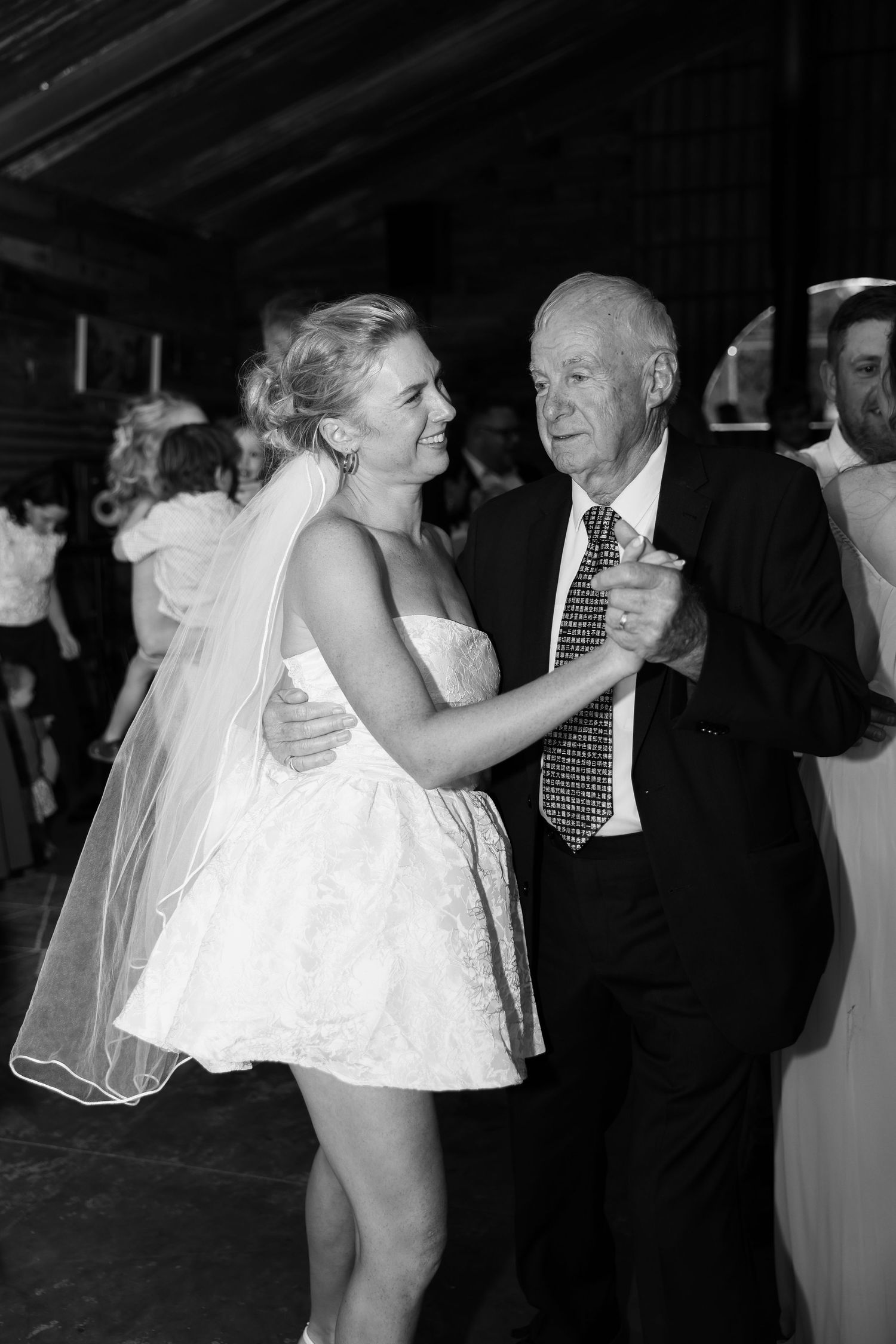 Black and white photo of bride in short dress dancing with elderly man at reception.