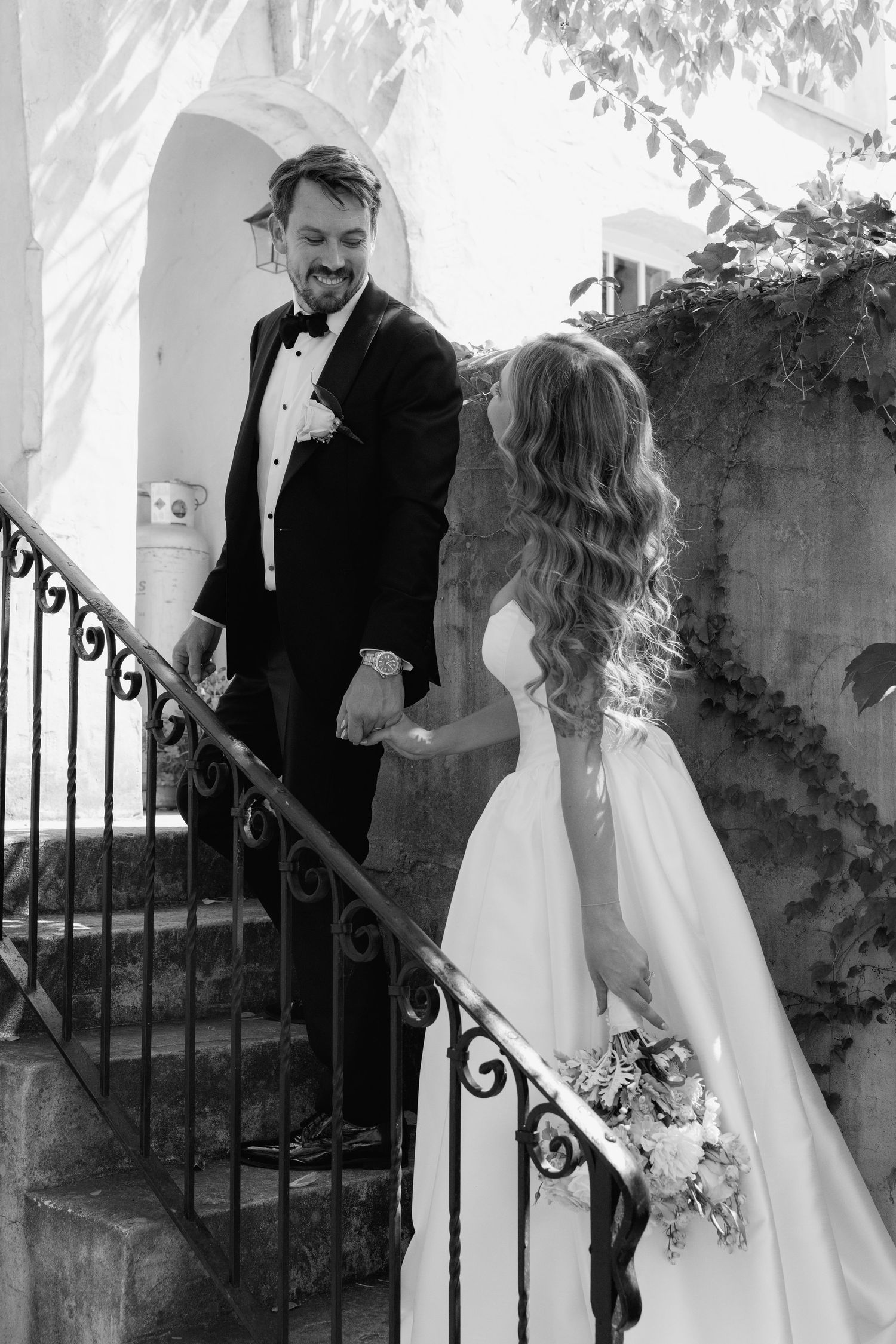 Black and white wedding photo of couple on vintage staircase with iron railing.