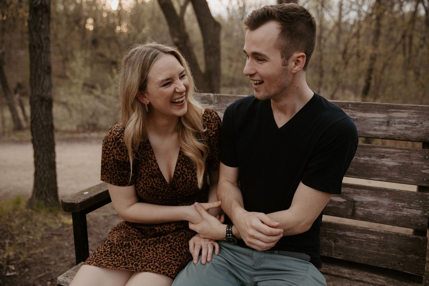 Young womenlaughs as she gazes at her fiance sitting on a bench