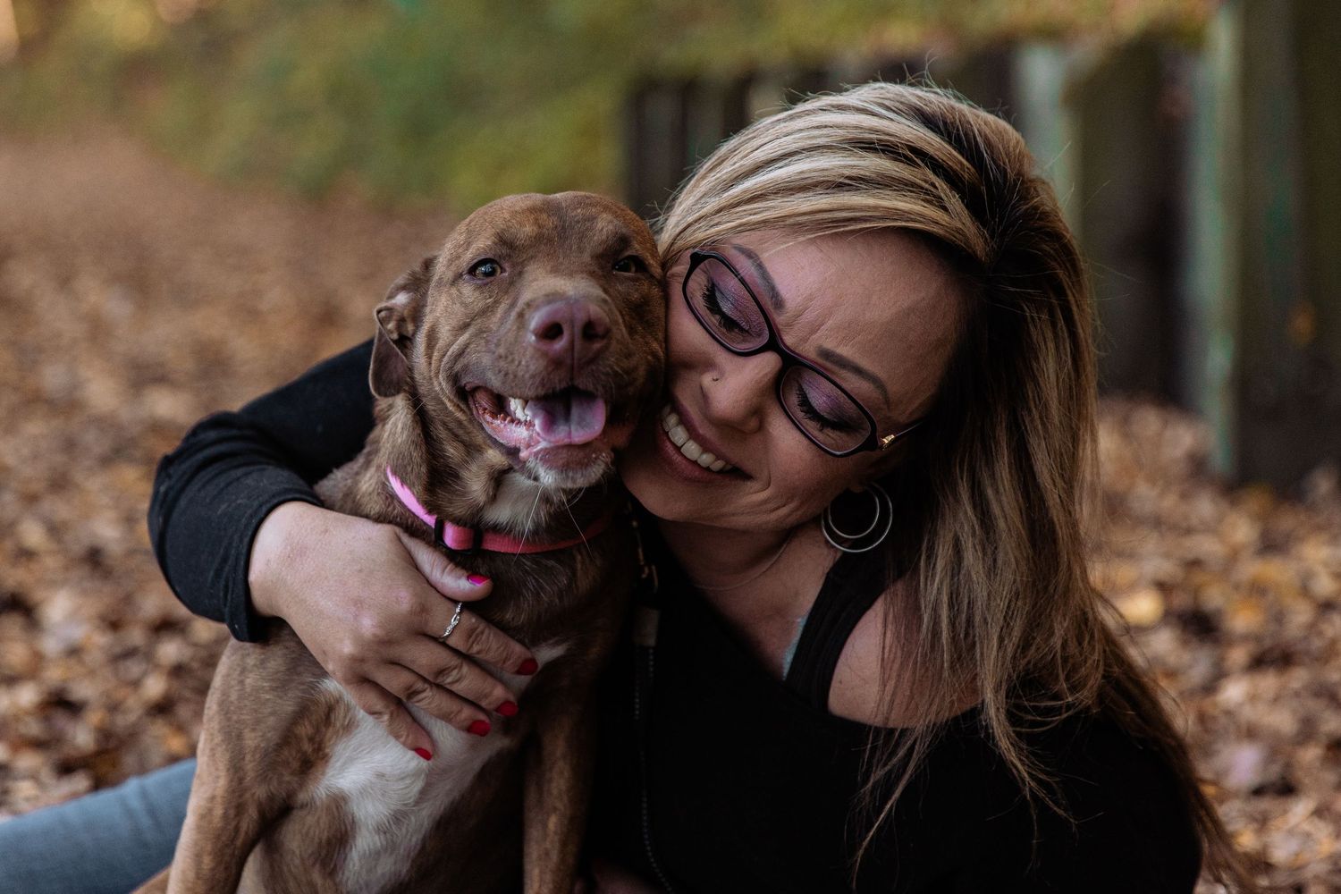 Young blonde woman gives her pitbull a big hug while they both smile at the camera