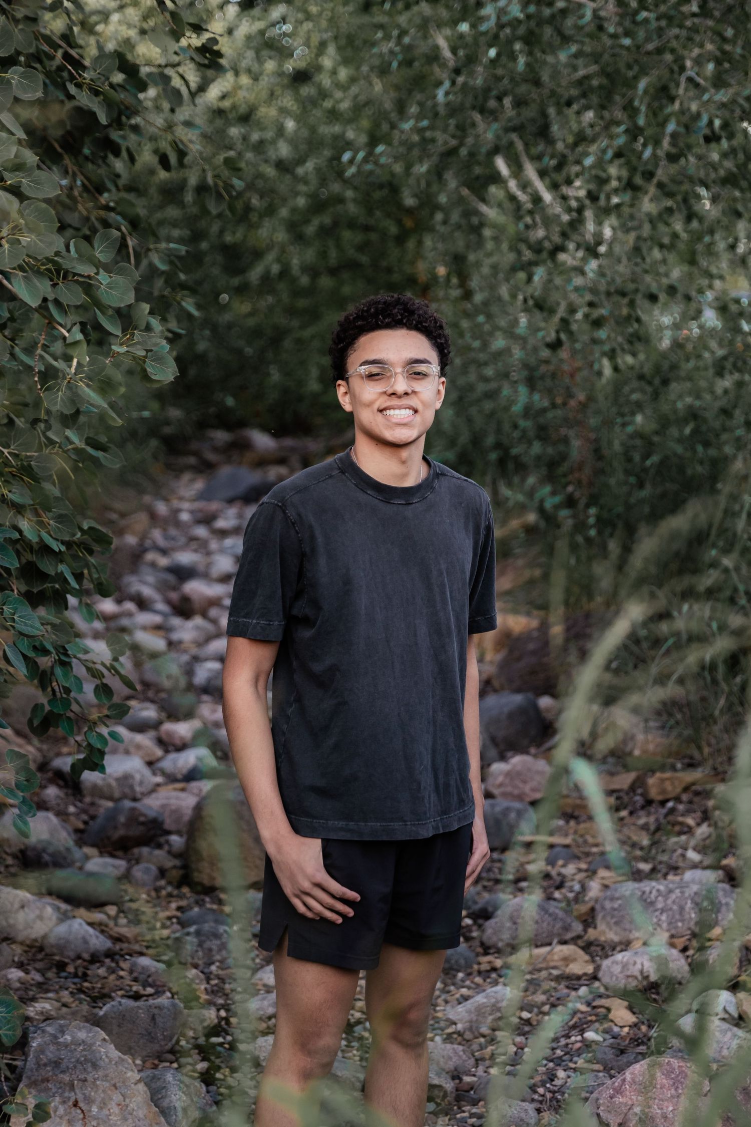 Farmington High School senior stands in a dried out creek bed surrounded by green leaves and colorful rocks
