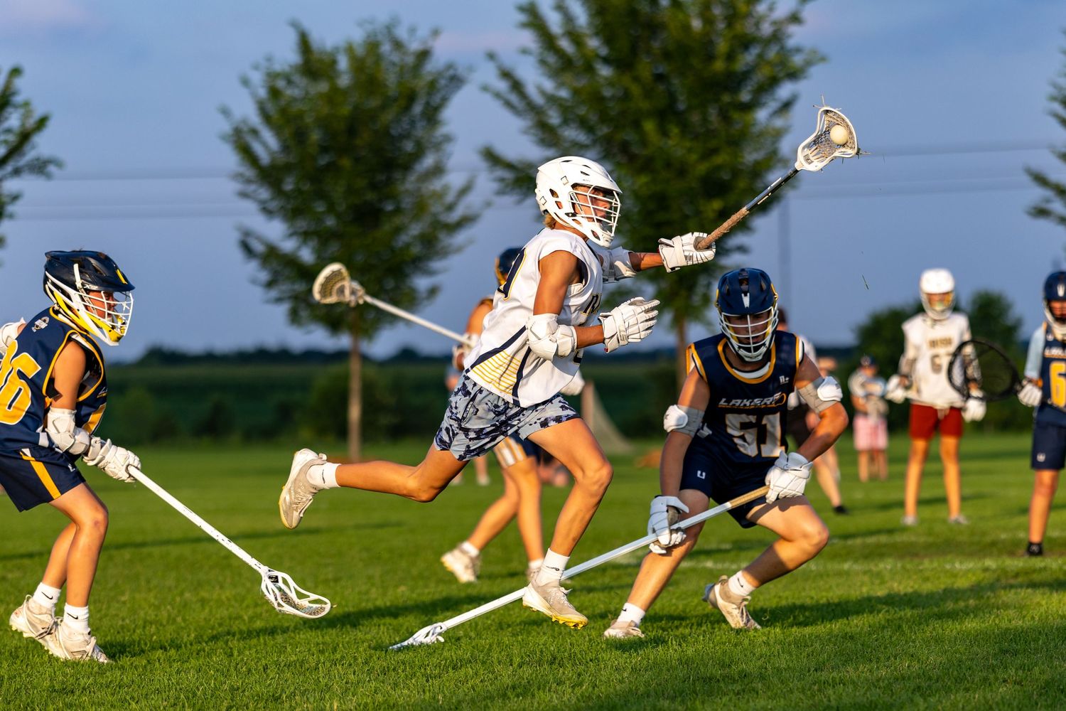 Youth lacrosse player jumps over a defender's stick to avoid losing the ball