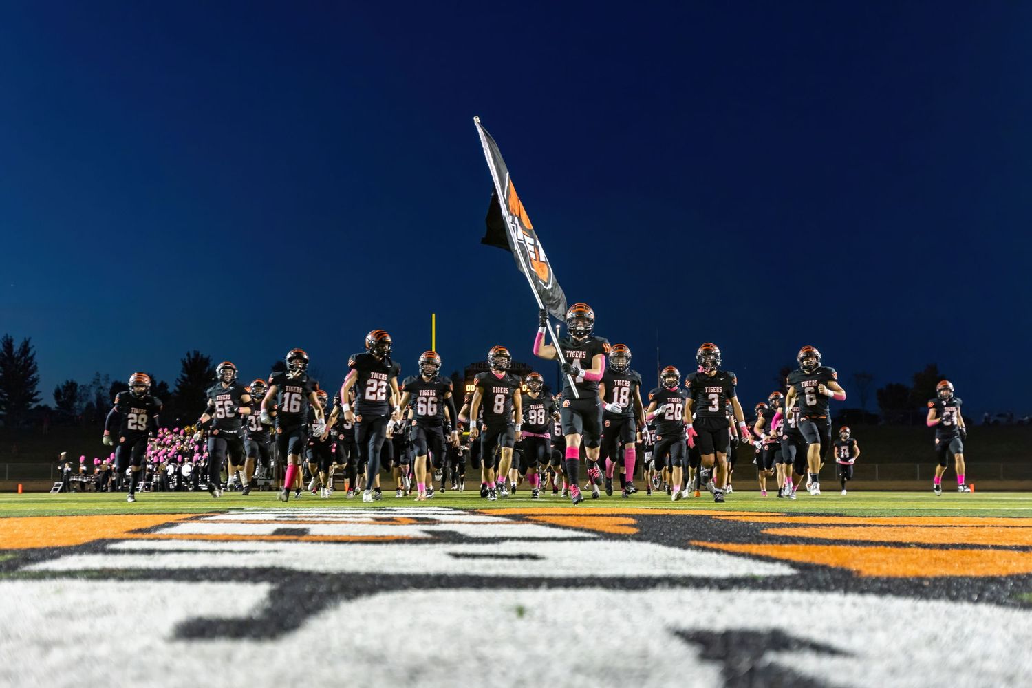Farmington Tigers varsity football team storms the field with their flag in hand