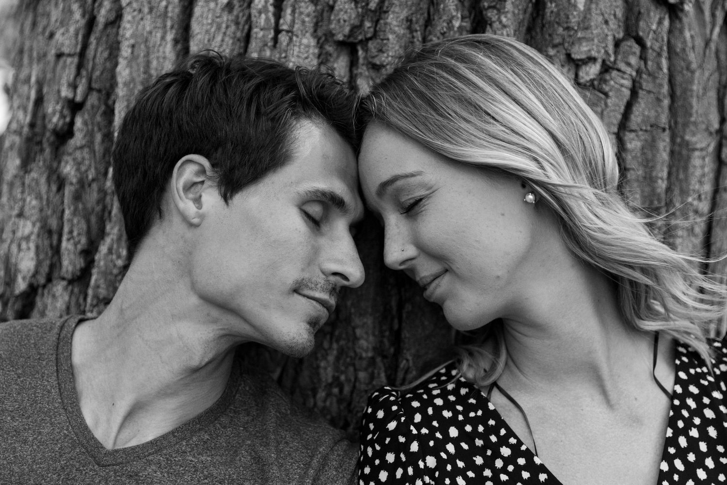 young couple softly touches foreheads as they cuddle up under an oak tree