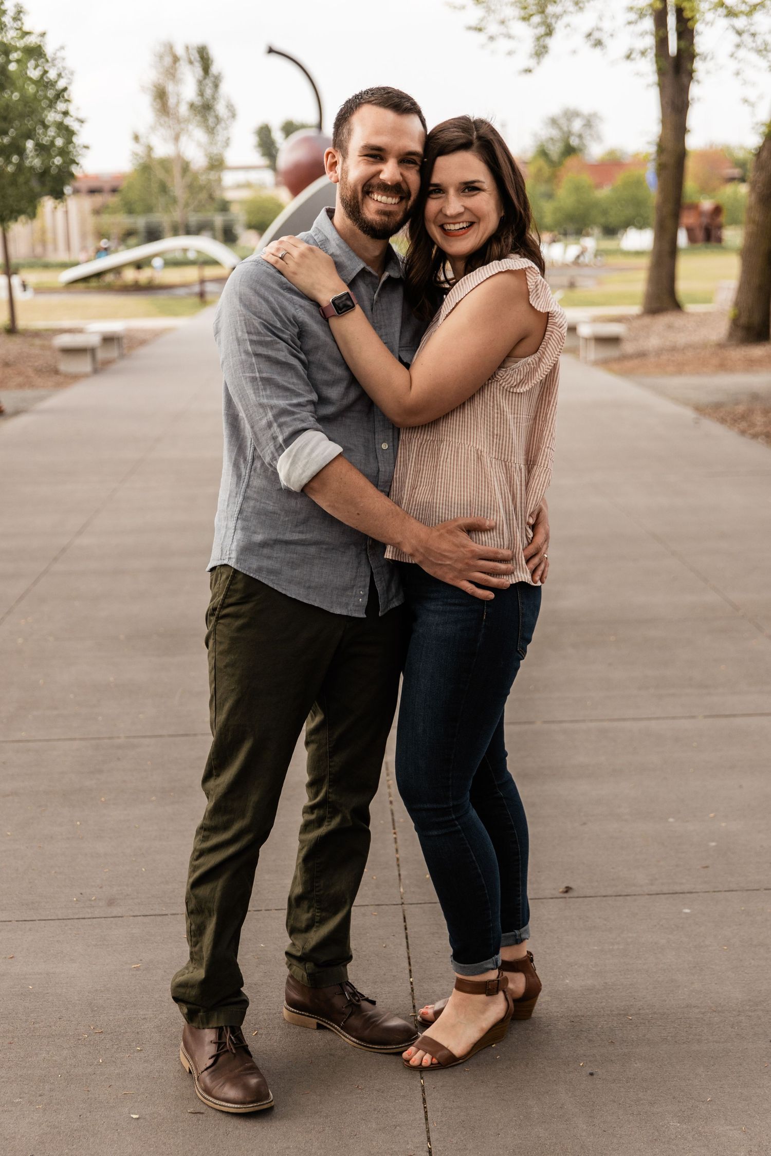 Husband and wife cozy up together as they stand embracing one another on a large concrete sidewalk