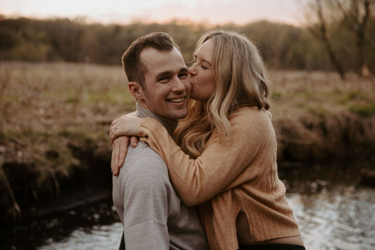 Young woman kisses her fiance on the cheek as they stand in a shallow creek