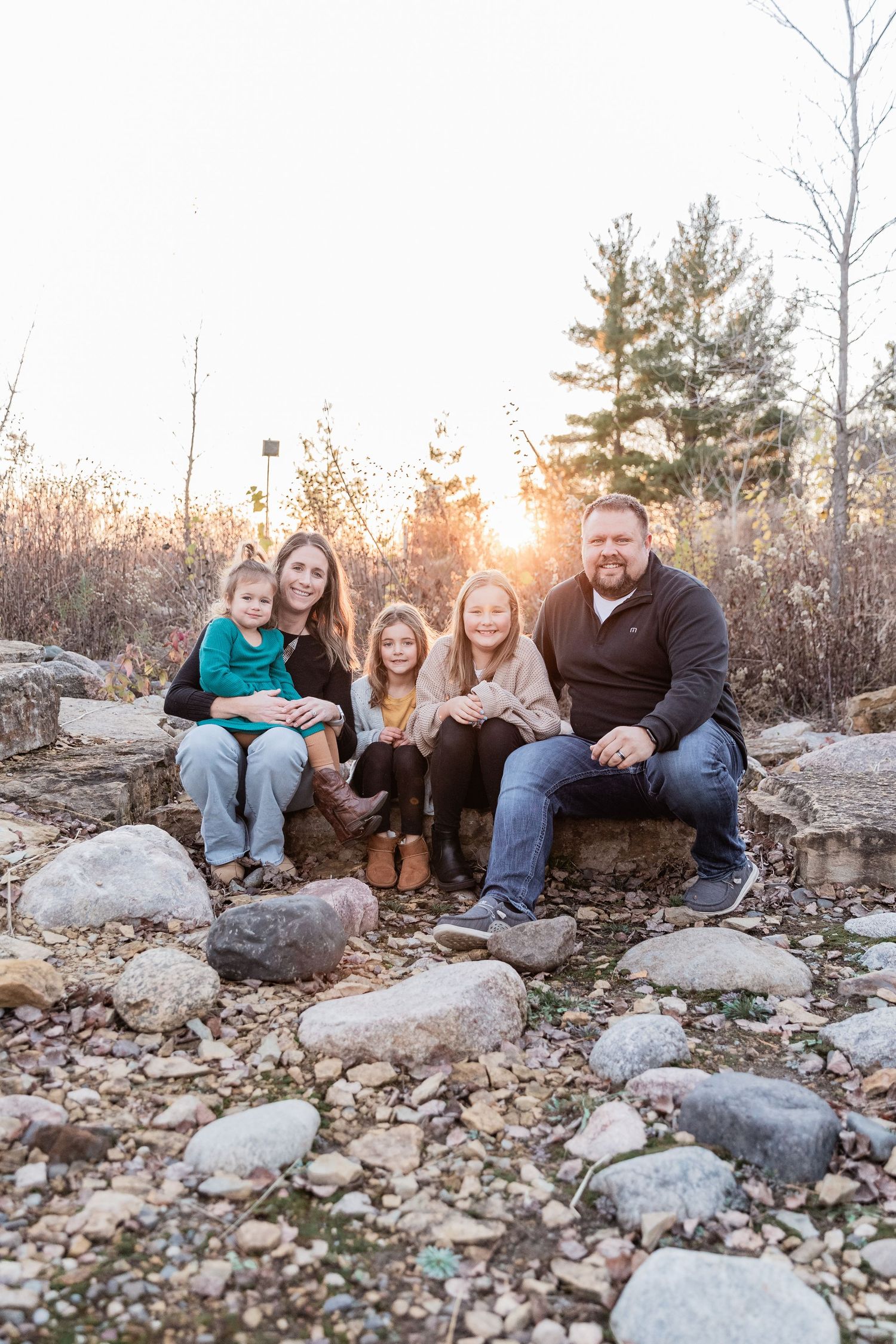 Hall family sitting on some large rocks as the sun sets behind the tall grass