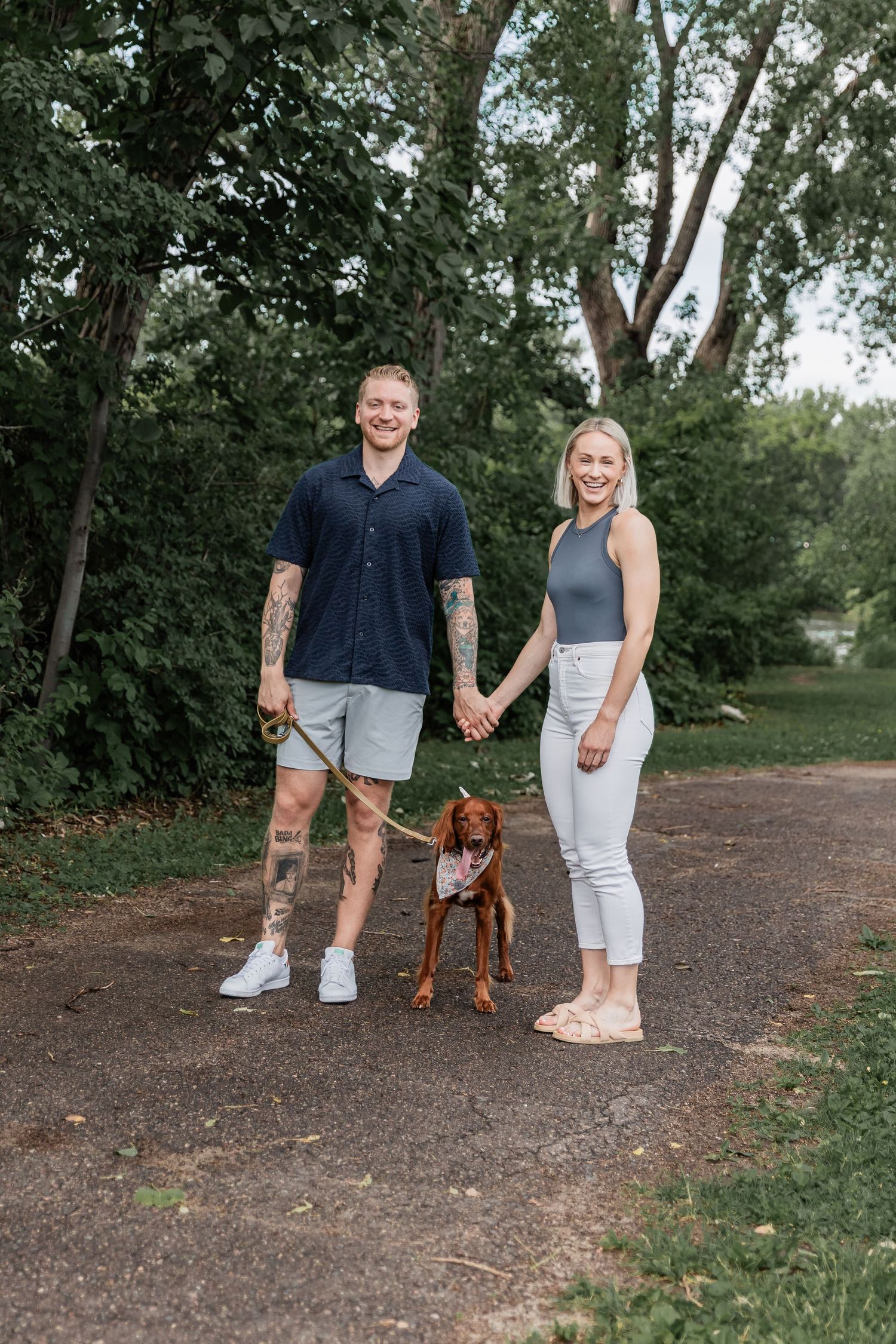 Young couple strolls down concrete path at Boom Island Park with their cocker spaniel