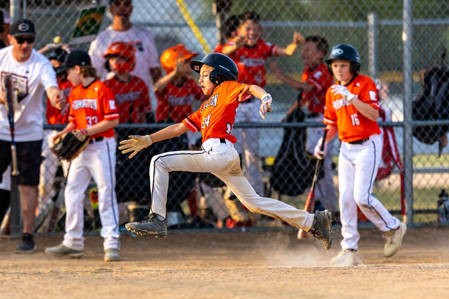Youth baseball player leaps over the ball to score a run at home